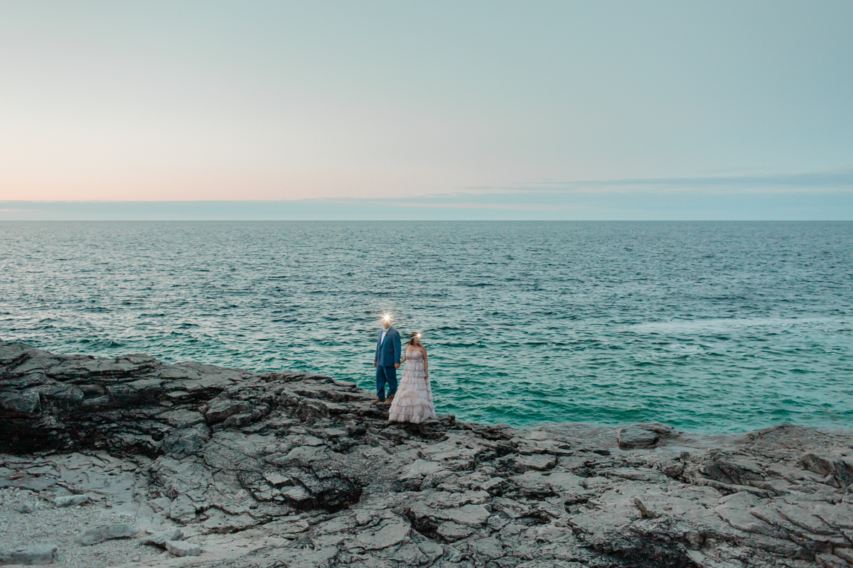 A sunset photo of a couple celebrating post vow ceremony exploring with headlamps on the rocks during their Ontario wedding