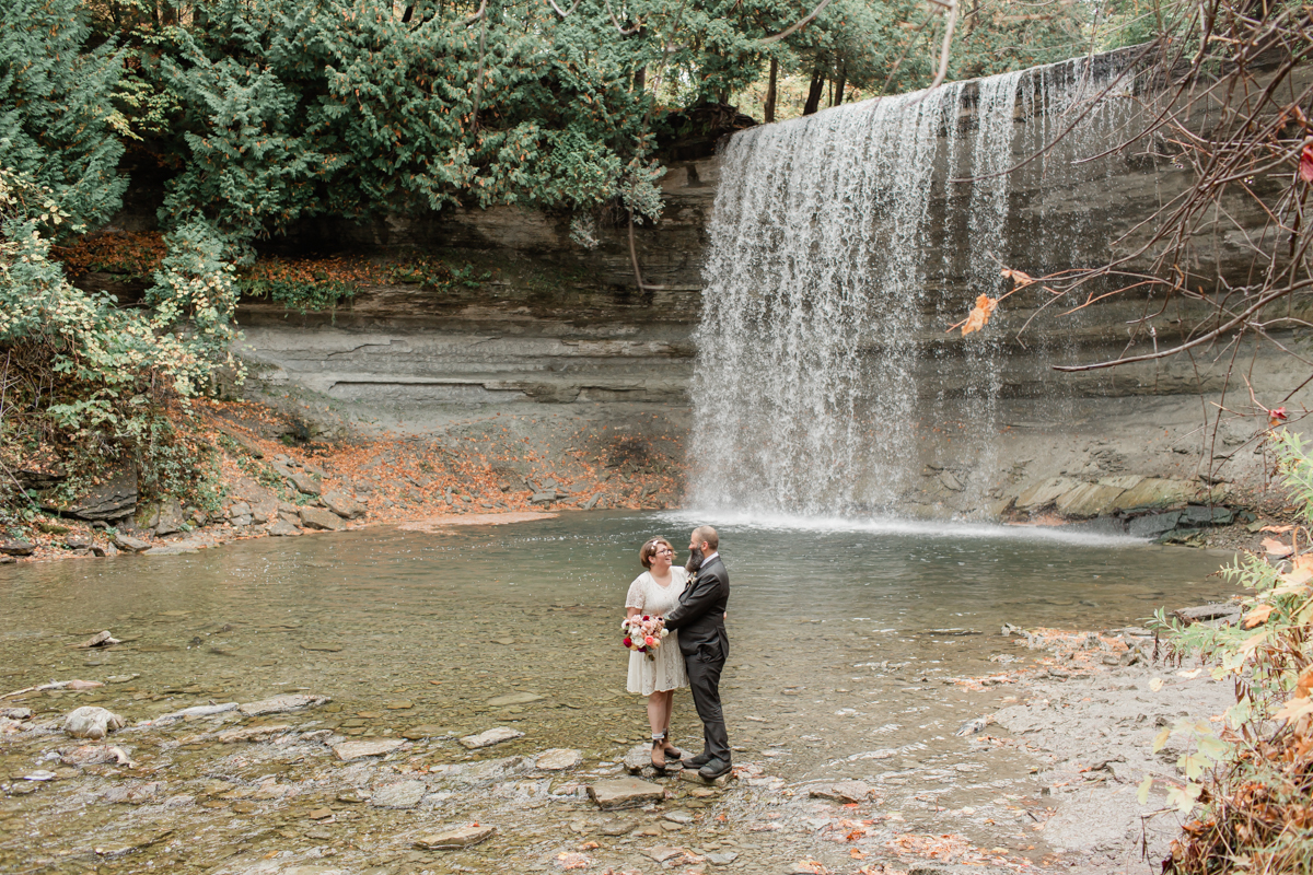 A couple embracing and laughing at Bridal Veil falls on Manitoulin island during their wedding 