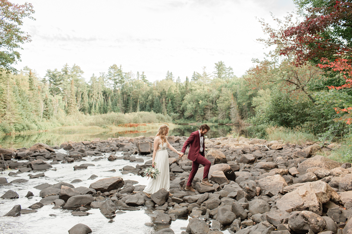 A couple walking along the lakeside rocks during their Ontario wedding