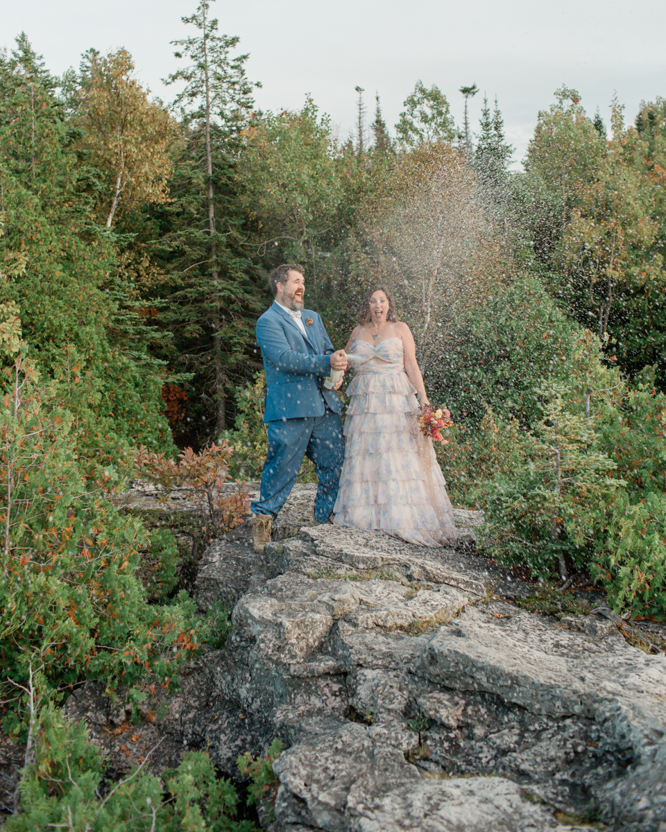 Katie and John pop champagne near the Grotto and Indian Head Cove for their Ontario elopement