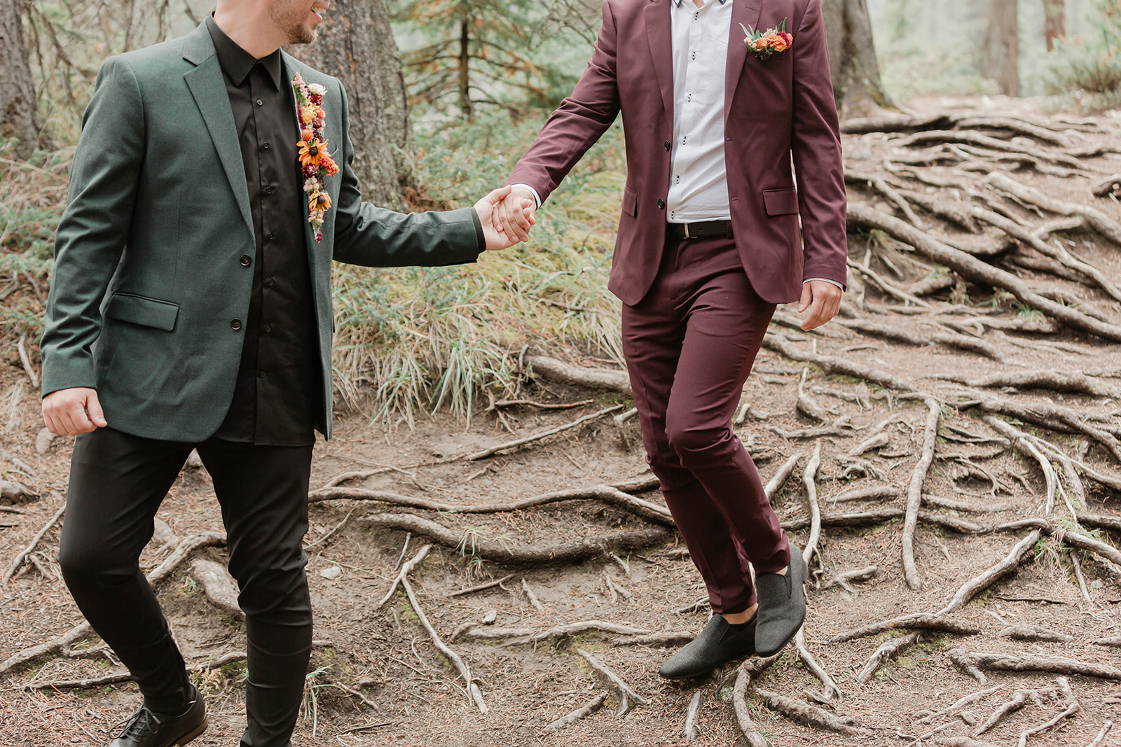 A man in a forest green suit leads his groom, who is wearing a burgundy suit, through Mistaya Canyon during their elopement.