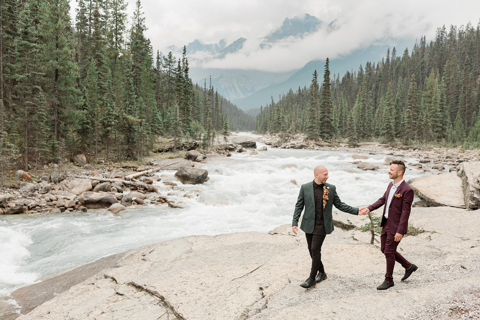 A Mistaya Canyon elopement couple walks along a rock formation while holding hands. 