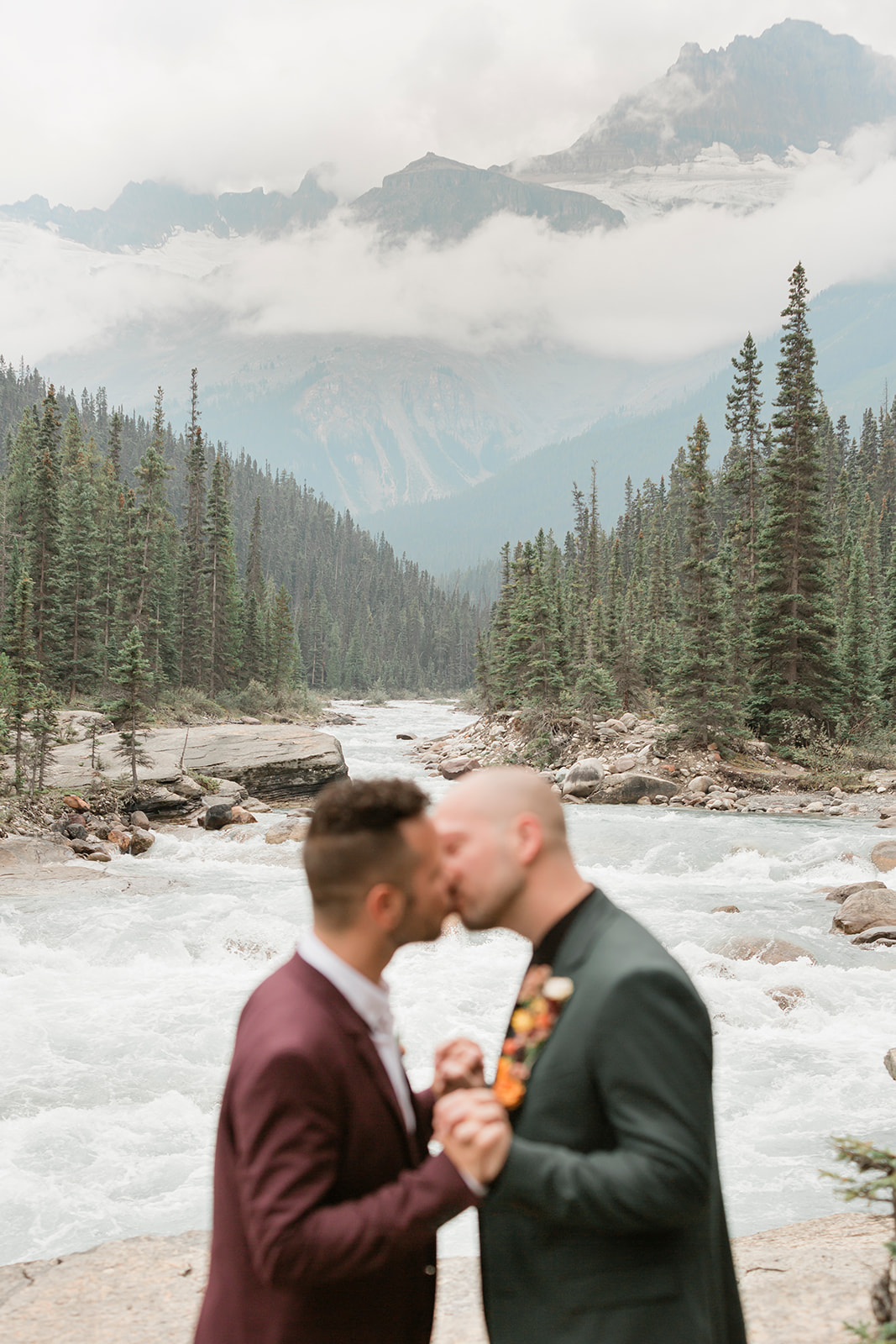 A Banff elopement couple kisses while embracing while holding hands near Mistaya Canyon. 