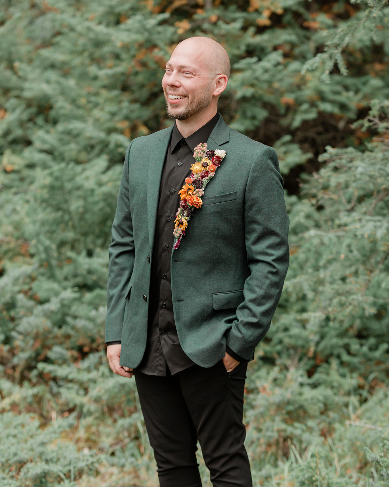 A groom in a forest green wedding suit with a colorful floral boutonniere on his lapel. 