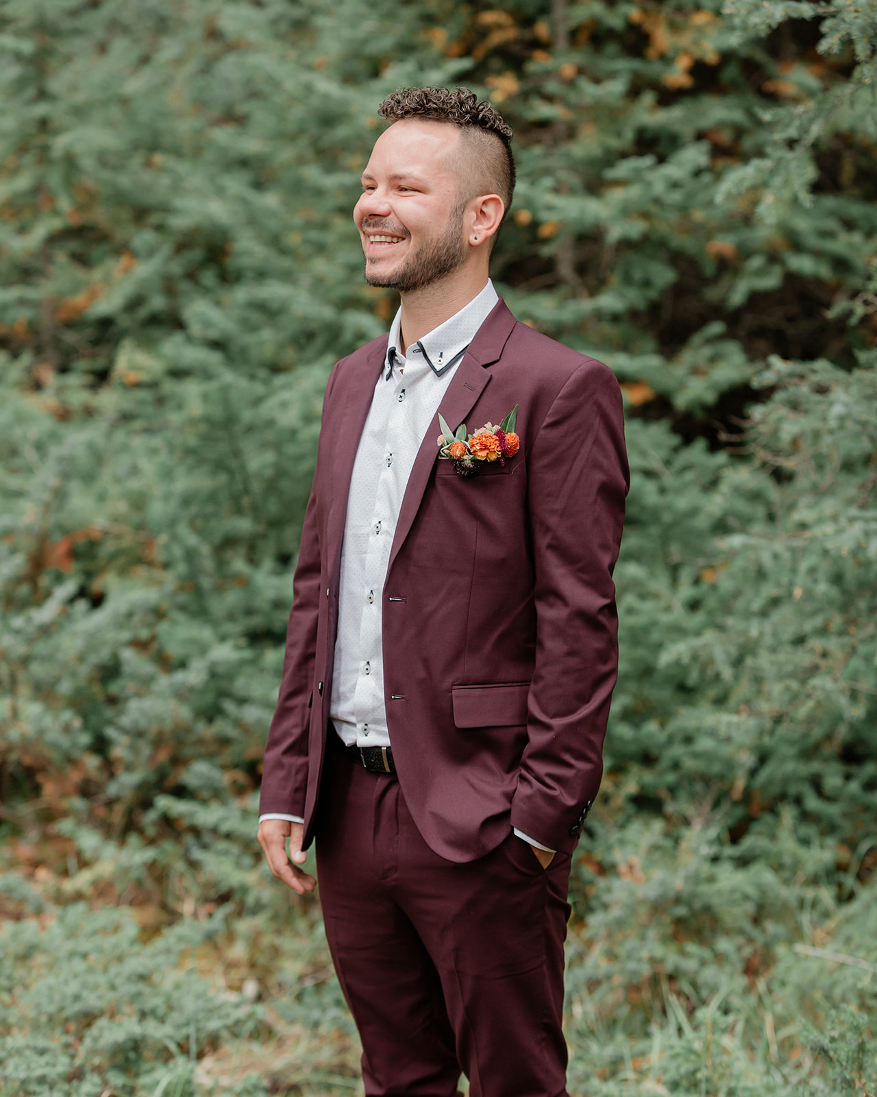 A groom in a for burgundy wedding suit with a colorful floral boutonniere on his lapel. 