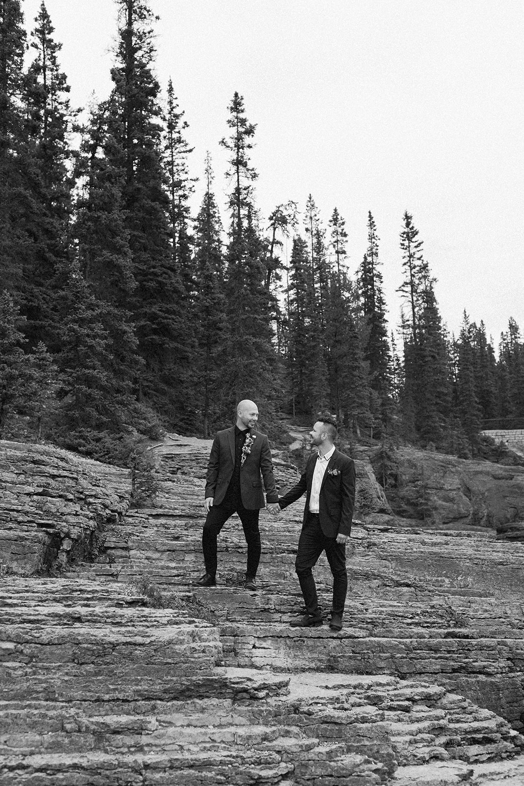 Grooms hold hands while standing on a rock formation near Mistaya Canyon. 