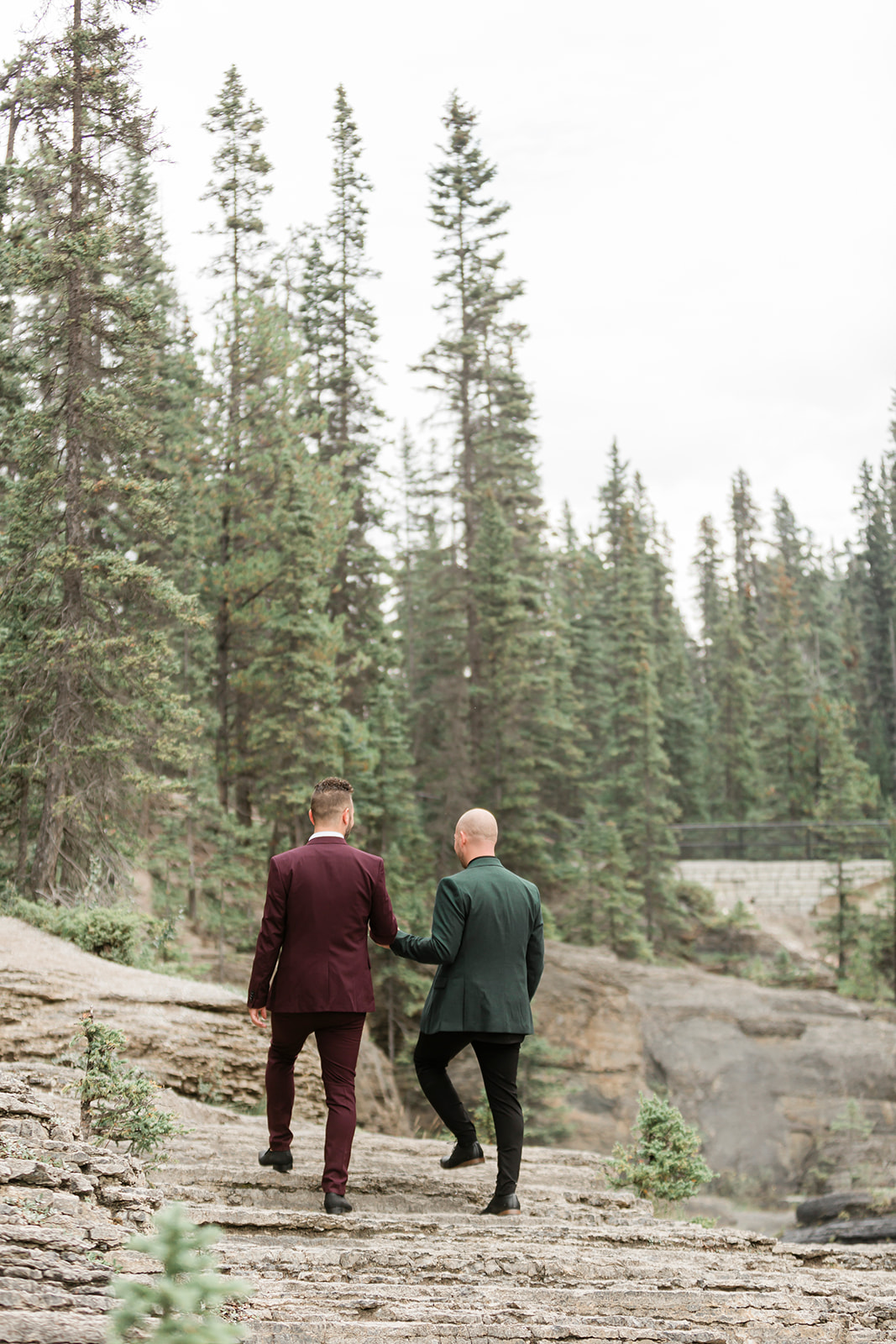 Grooms hold hands while walking along a rock formation near Mistaya Canyon. 