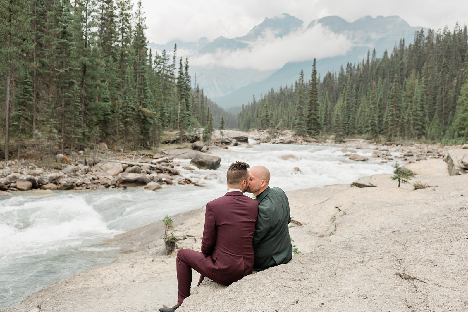 An elopement couple kisses while sitting on a rock formation that overlooks Mistaya Canyon.