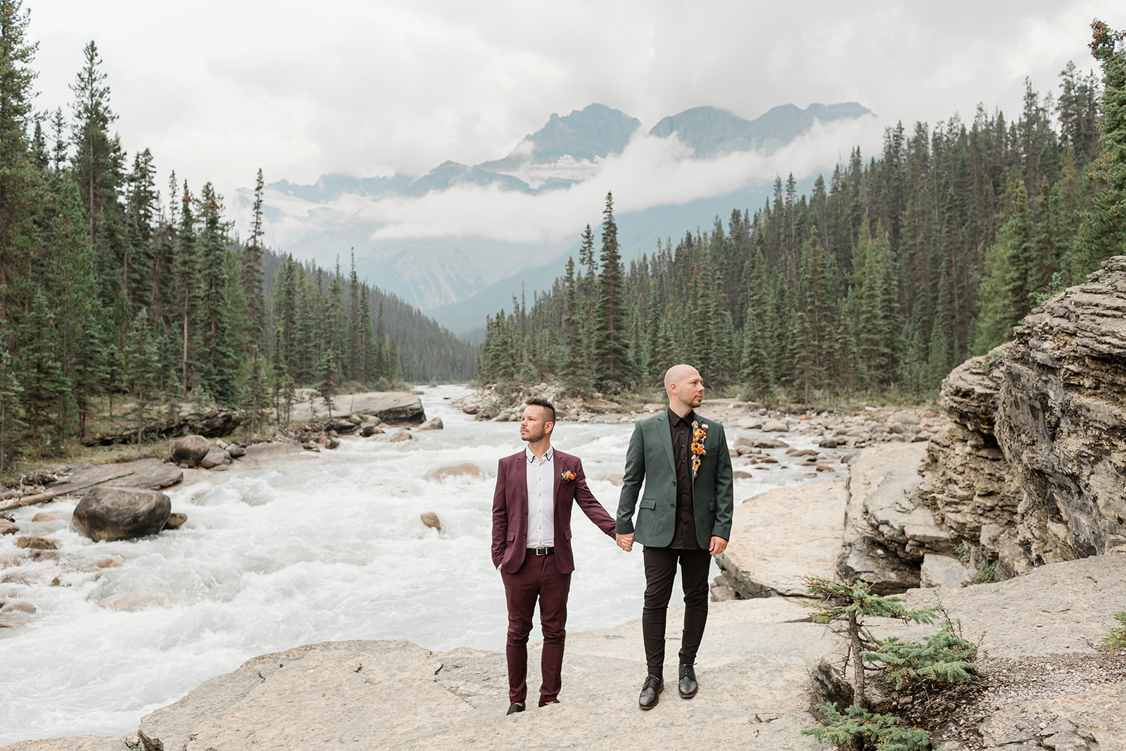 A couple in formal wedding attire holds hands near Mistaya Canyon while taking an outdoor wedding portrait.