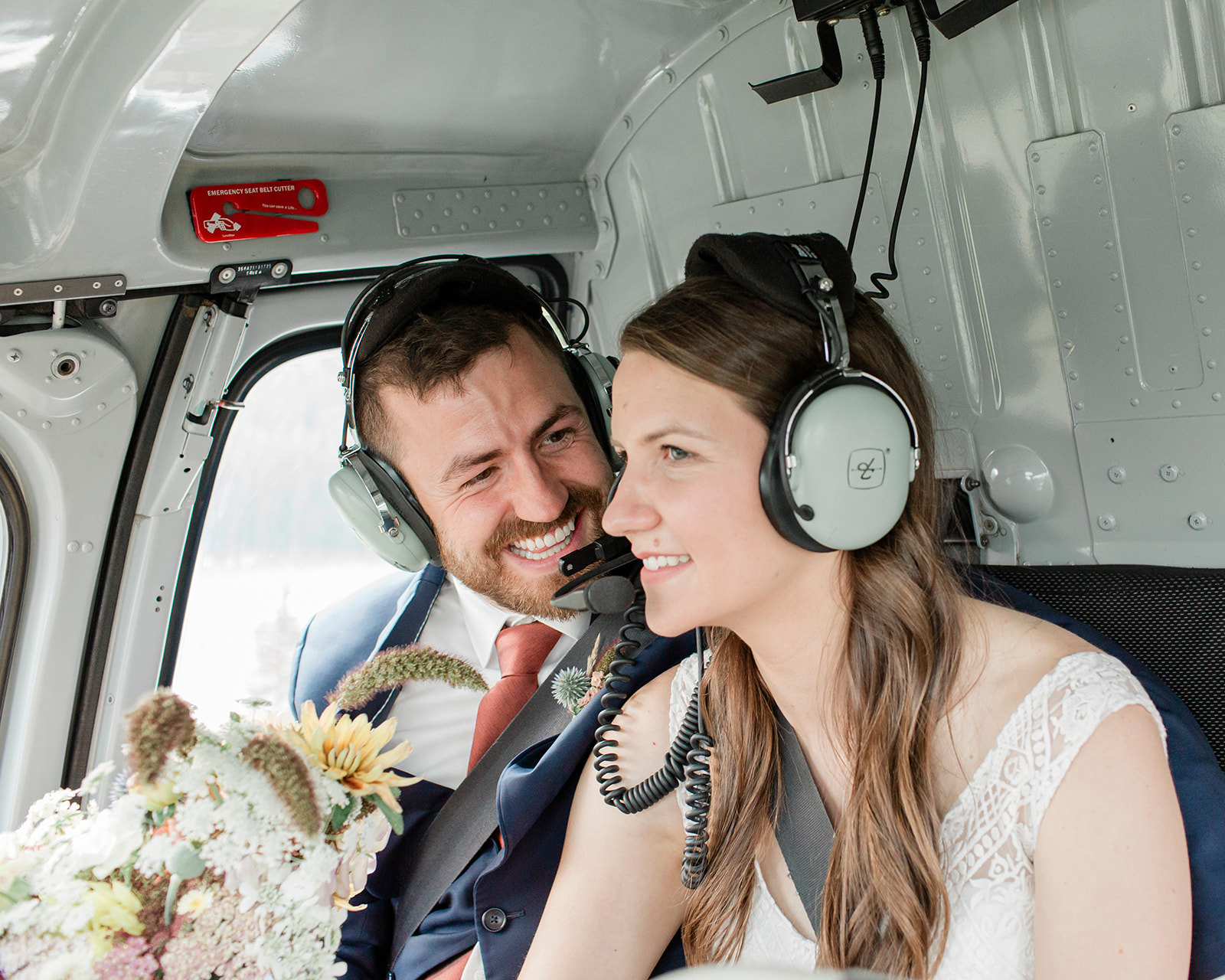 A groom smiles at his bride while riding in a Rockies Heli helicopter during a Banff helicopter wedding.