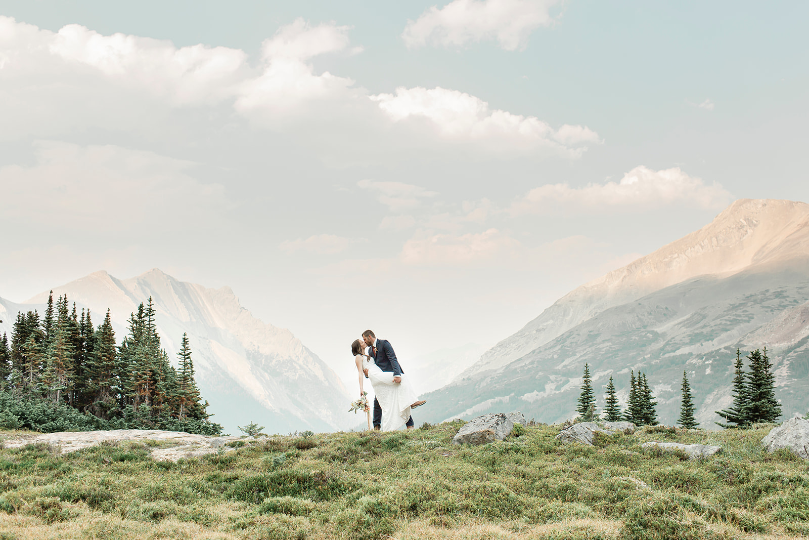 A Banff elopement couple kisses while on a grassy overlook during their vow ceremony. 