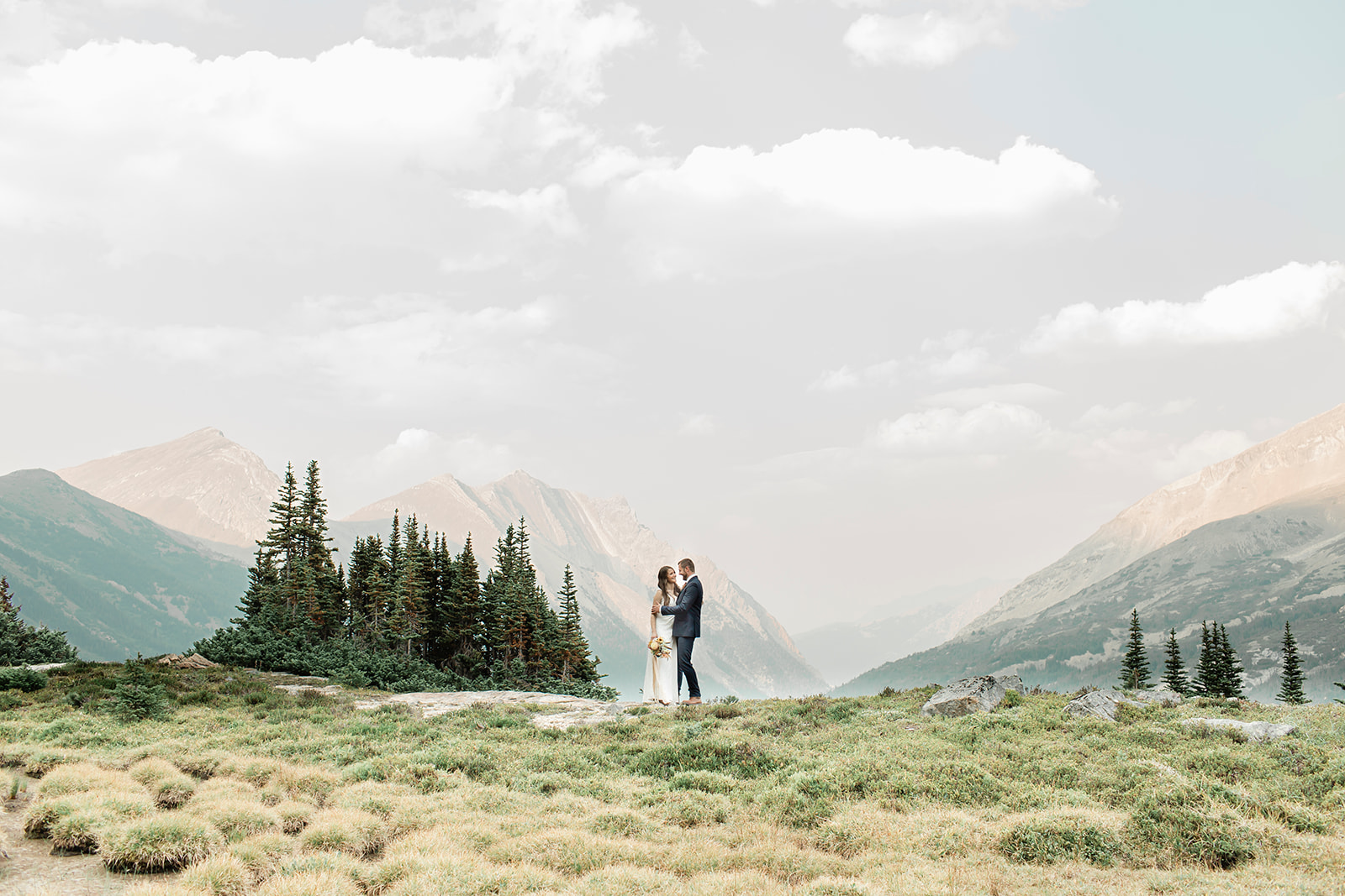 A couple in formal wedding attire embraces with mountains in the background during their Banff elopement. 