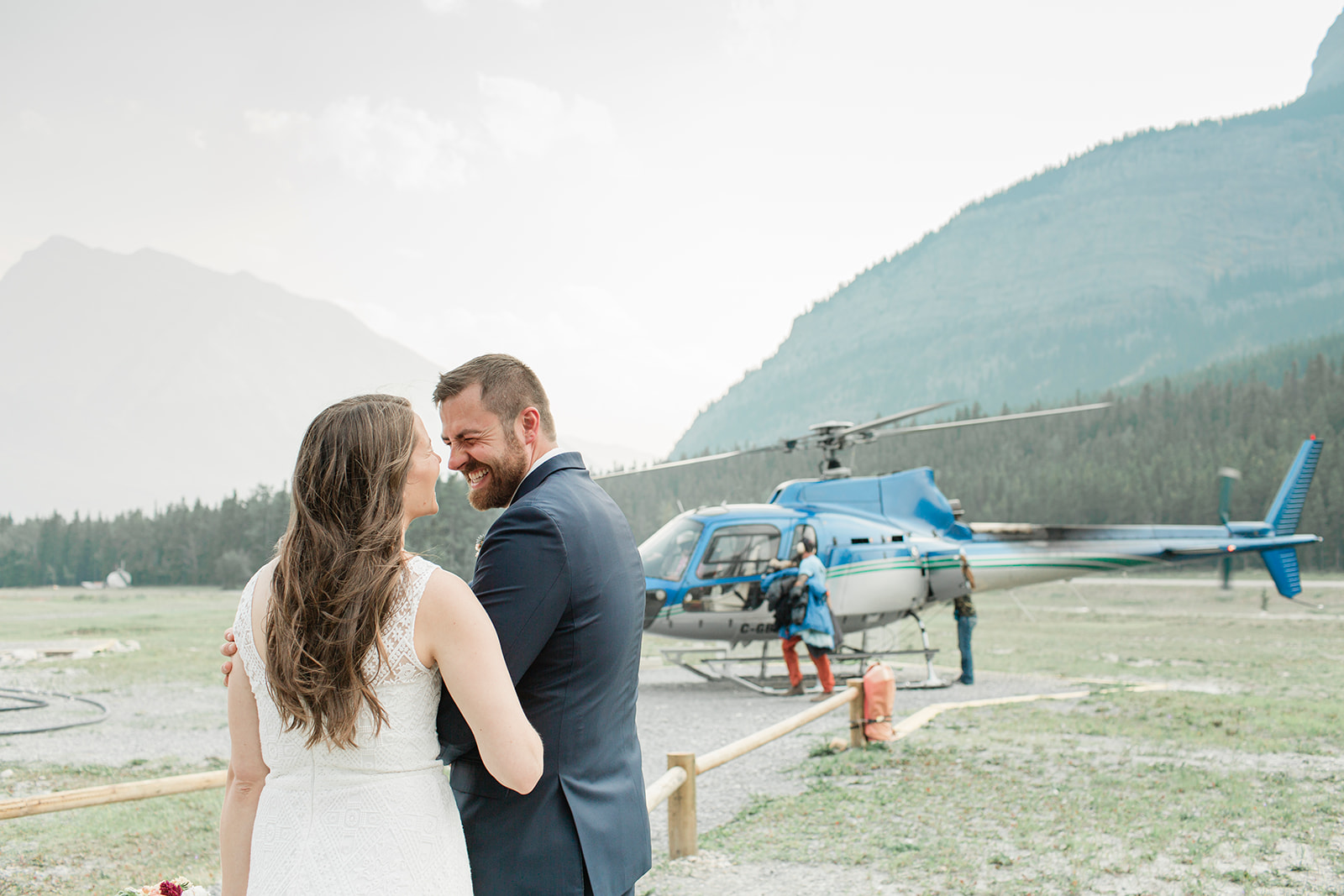 A Banff elopement couple shares a laugh near a helicopter just before their flight. 