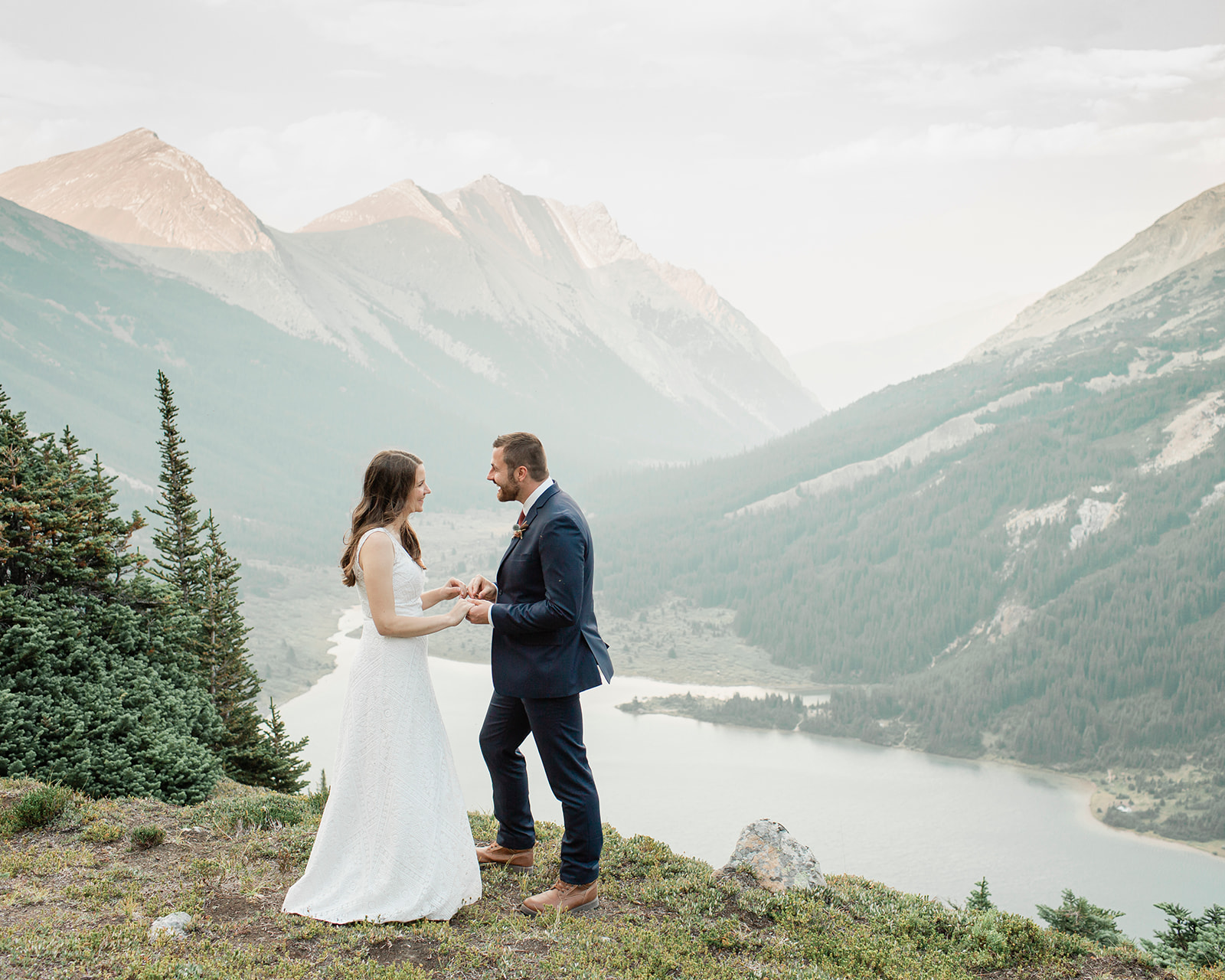 A Banff helicopter wedding couple holds hands with one another during their ceremony overlooking an alpine lake. 