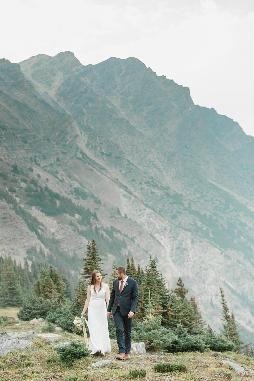 A helicopter elopement couple holds hands while wandering around Banff.