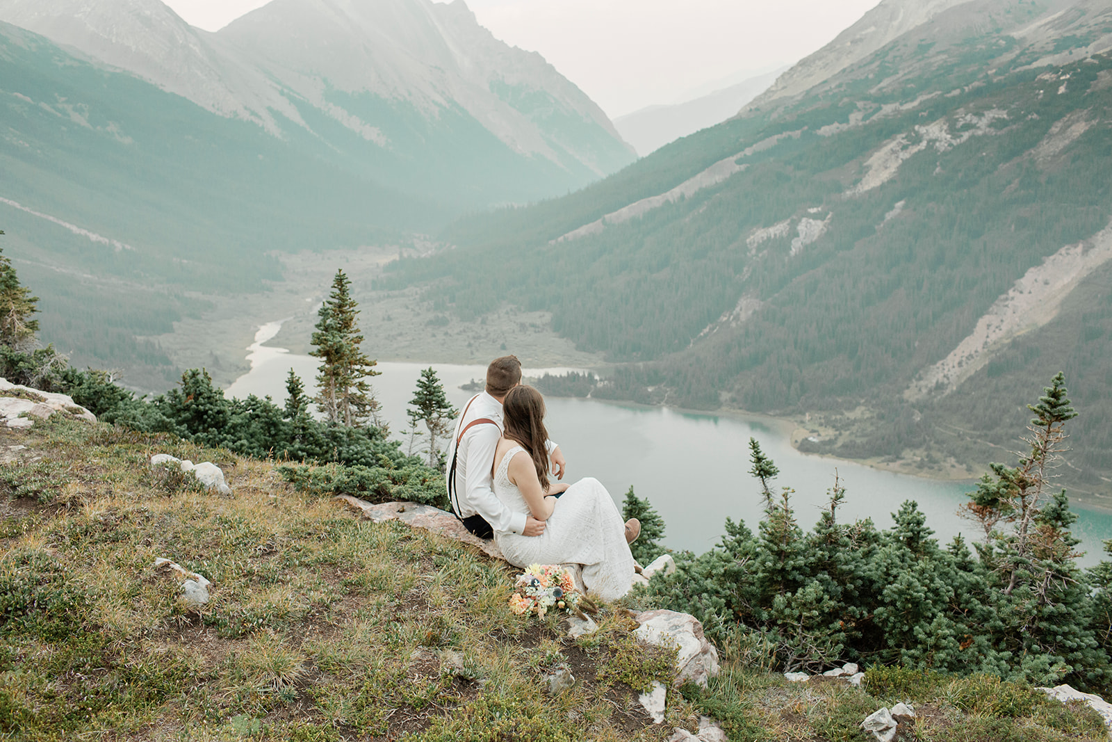 A couple sits and admires an alpine lake near Banff National Park during their helicopter elopement. 