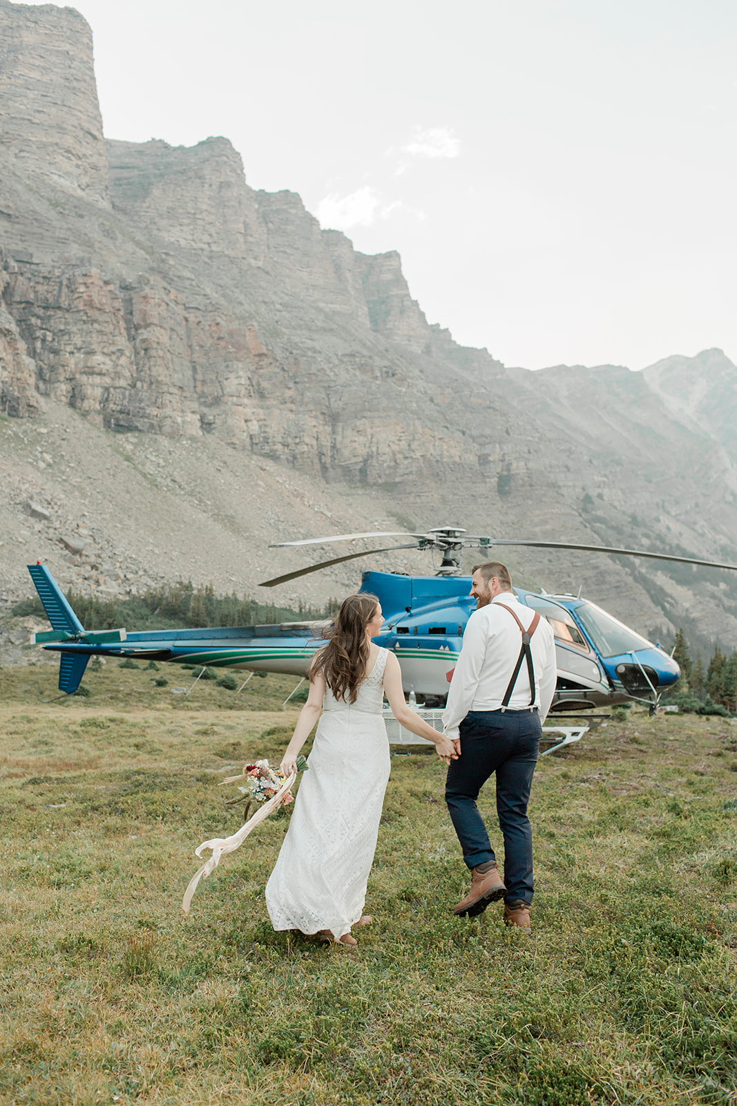 A helicopter elopement couple walks towards a RockiesHeli helicopter.