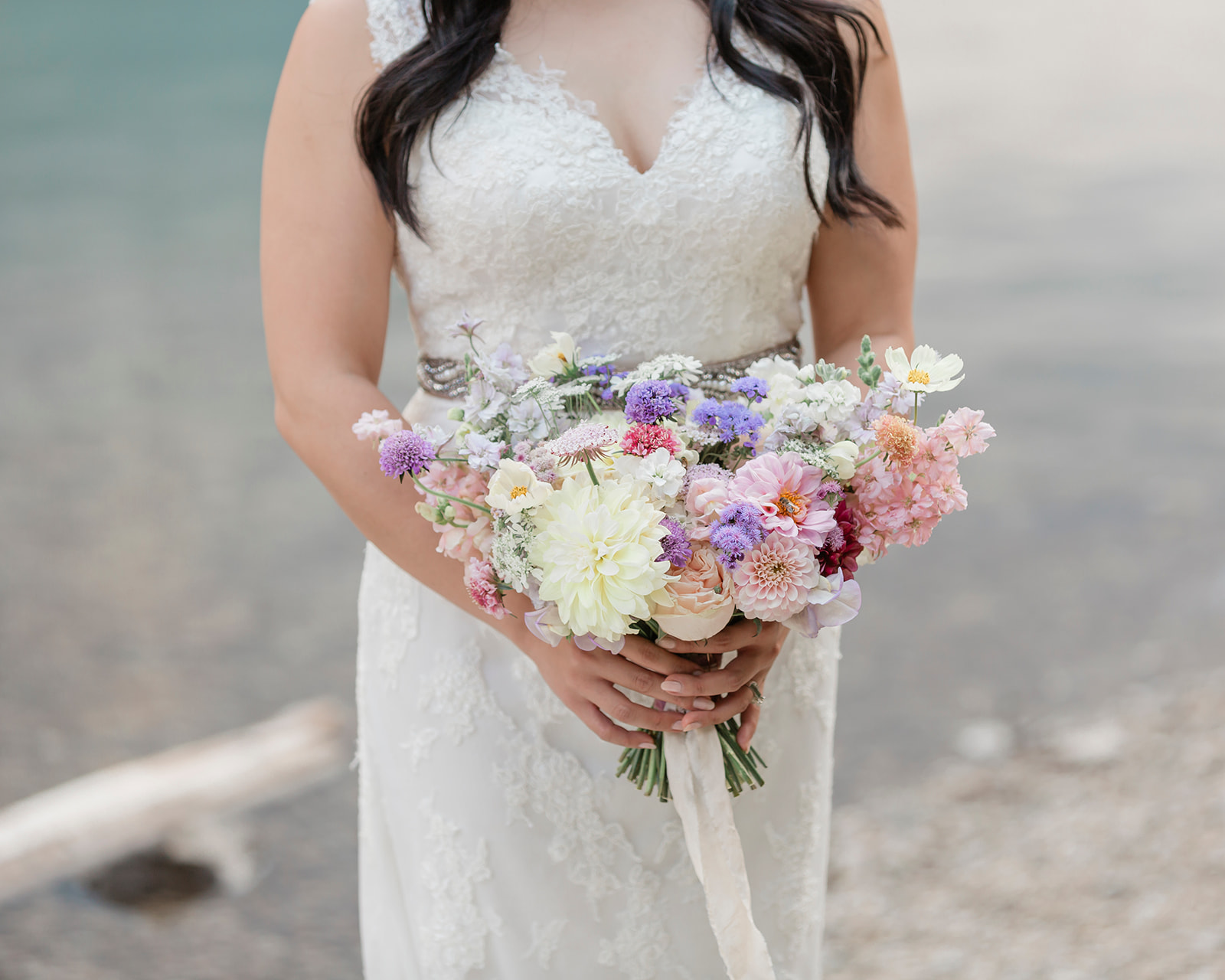 A bride in a white, lace wedding gown holds a bright, pastel bouquet during her Banff elopement. 