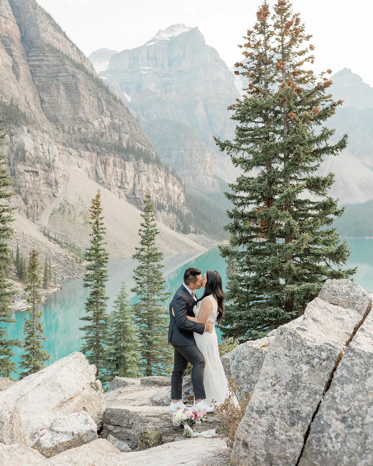 A Banff elopement couple in formal wedding attire embraces while kissing during their lakeside vow ceremony. 