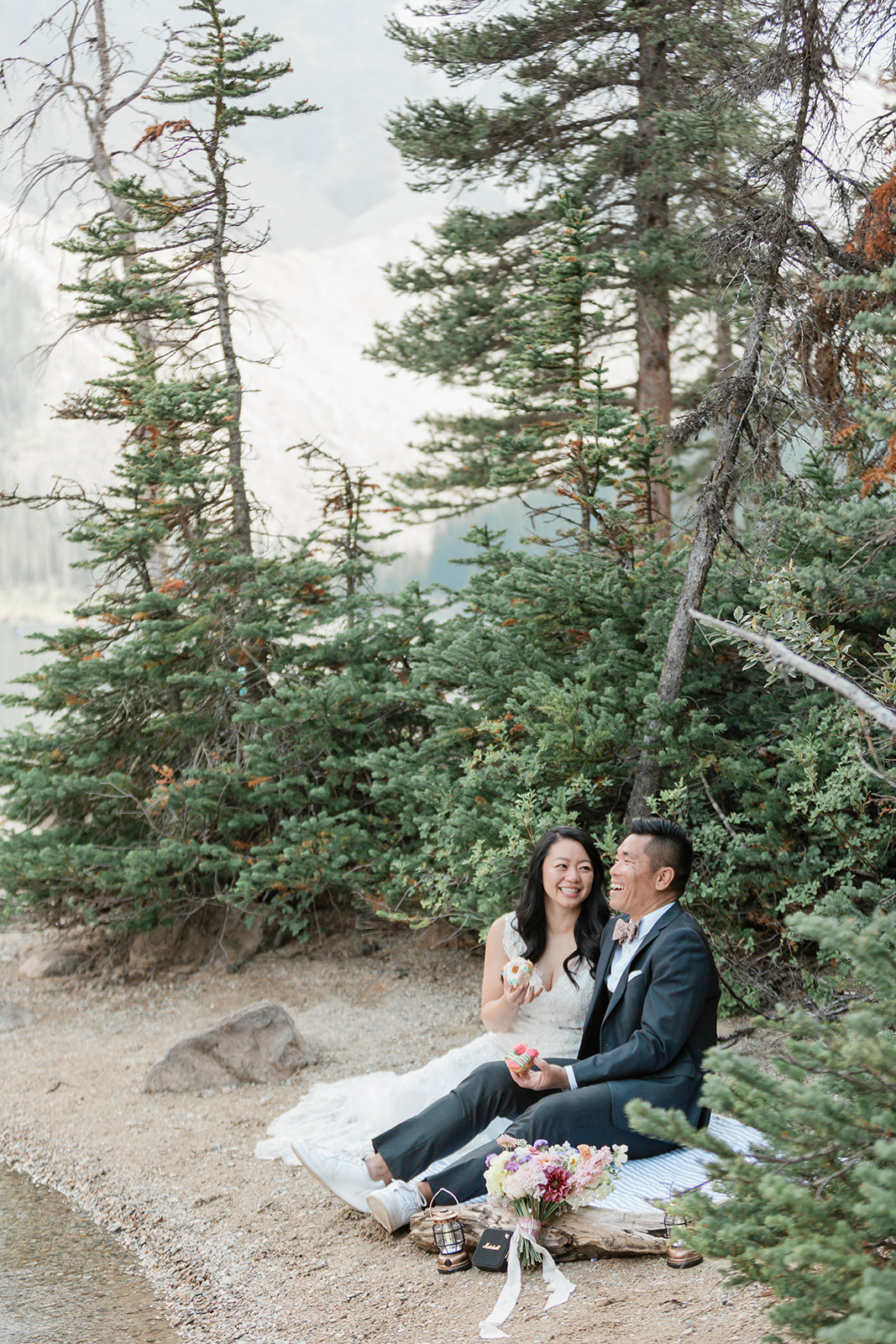 A couple in formal wedding attire shares a lakeside picnic in Banff National Park. 