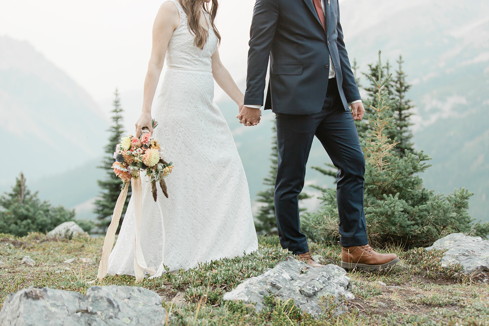 A Banff elopement couple dressed in formal wedding attire holds hands while walking through Banff. 