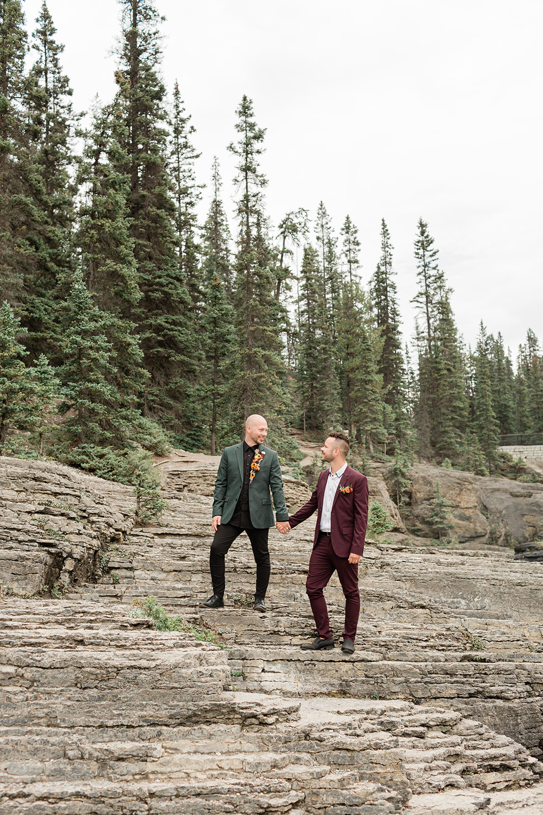 A Mistaya Canyon elopement couple holds hands while standing atop a rock formation. 