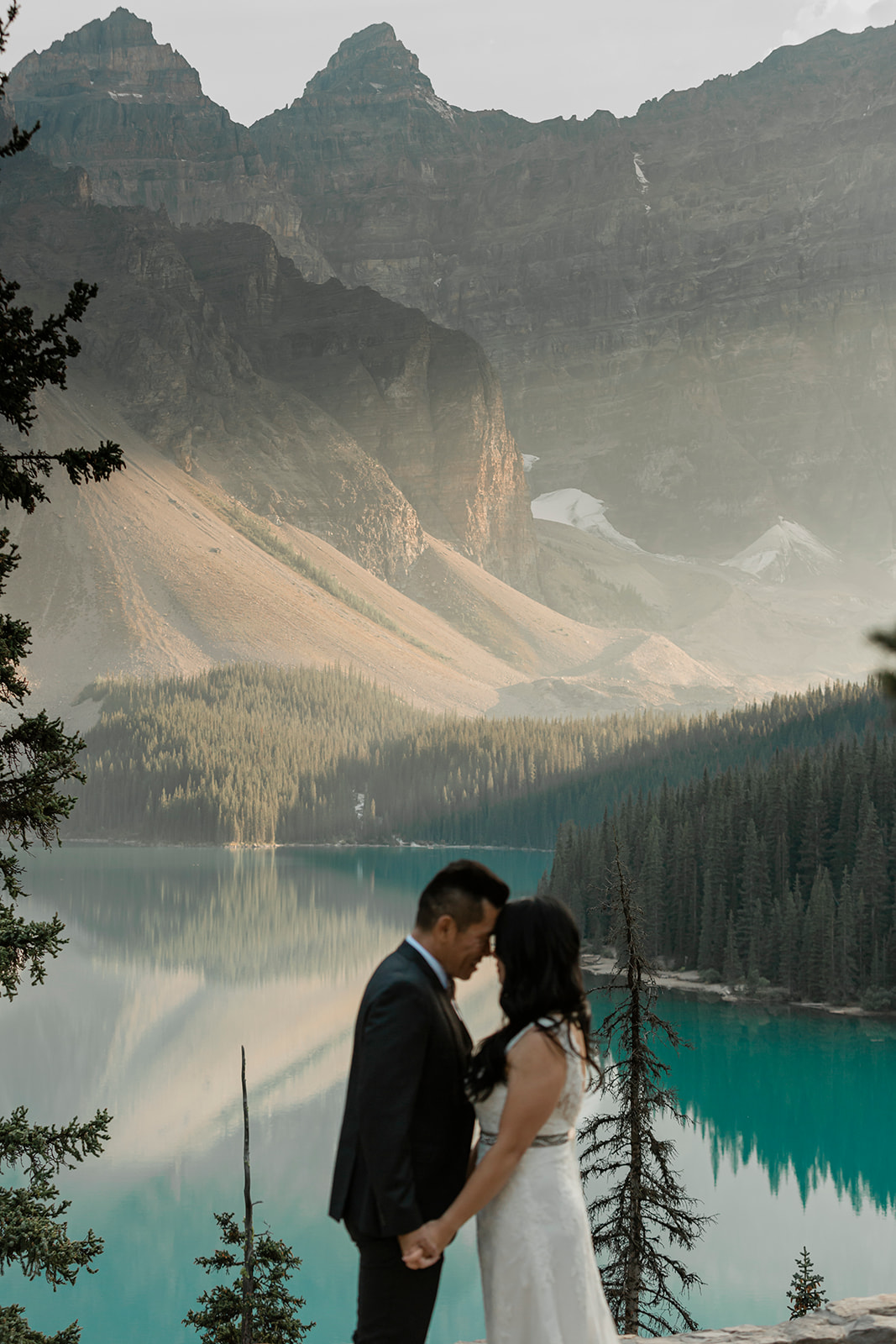 A couple in formal wedding attire hugs during their vow ceremony near an alpine lake in Banff National Park. 