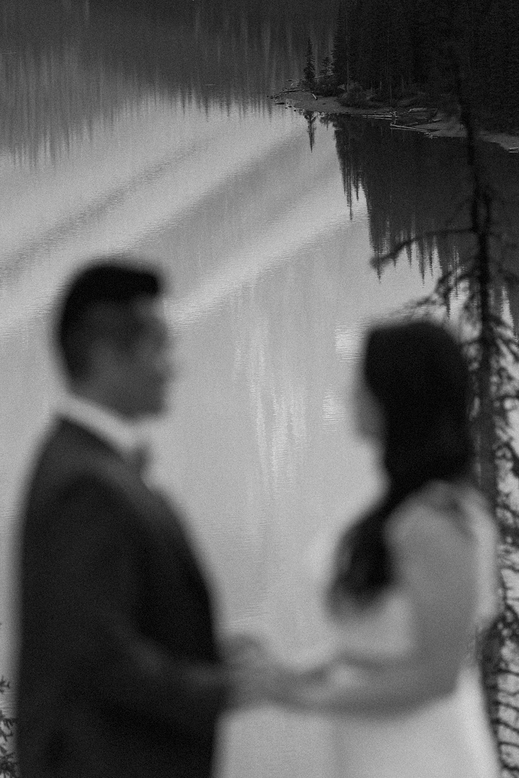 A couple in formal wedding attire holds hands during their vow ceremony near an alpine lake in Banff National Park. 