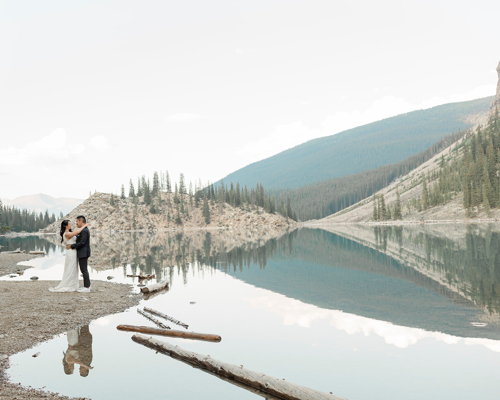 A couple in formal wedding attire embraces during their outdoor elopement near an alpine lake in Banff National Park. 