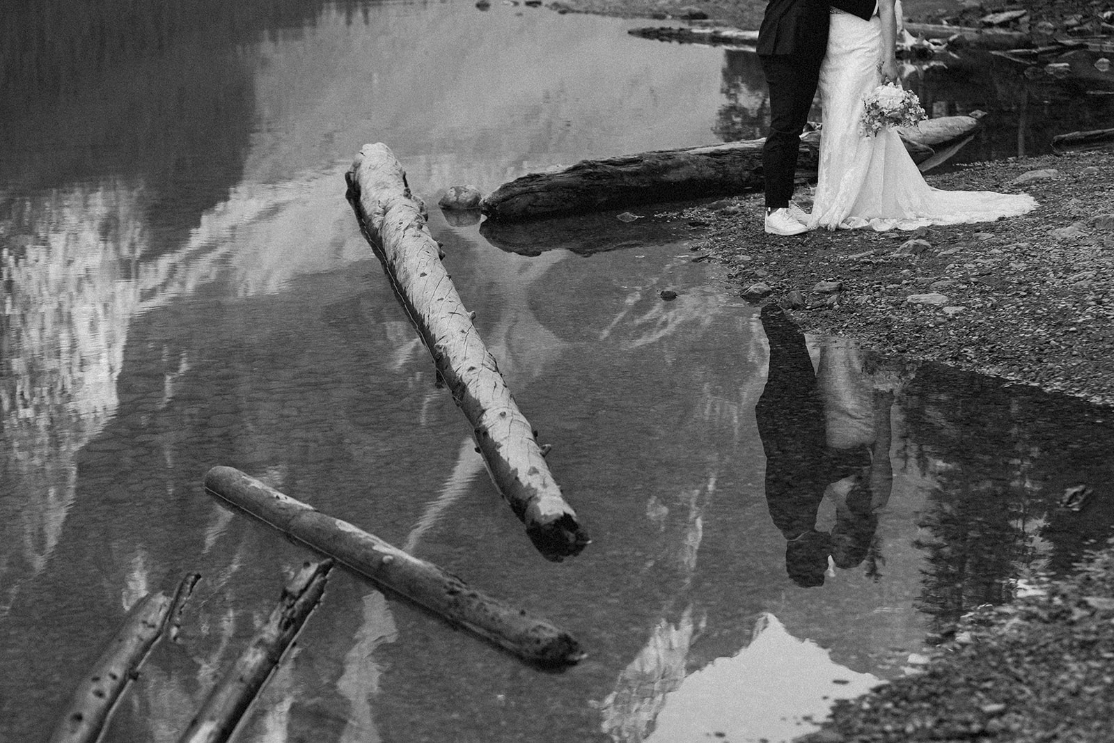 A bride and groom's reflection in an alpine lake in Banff National Park. 