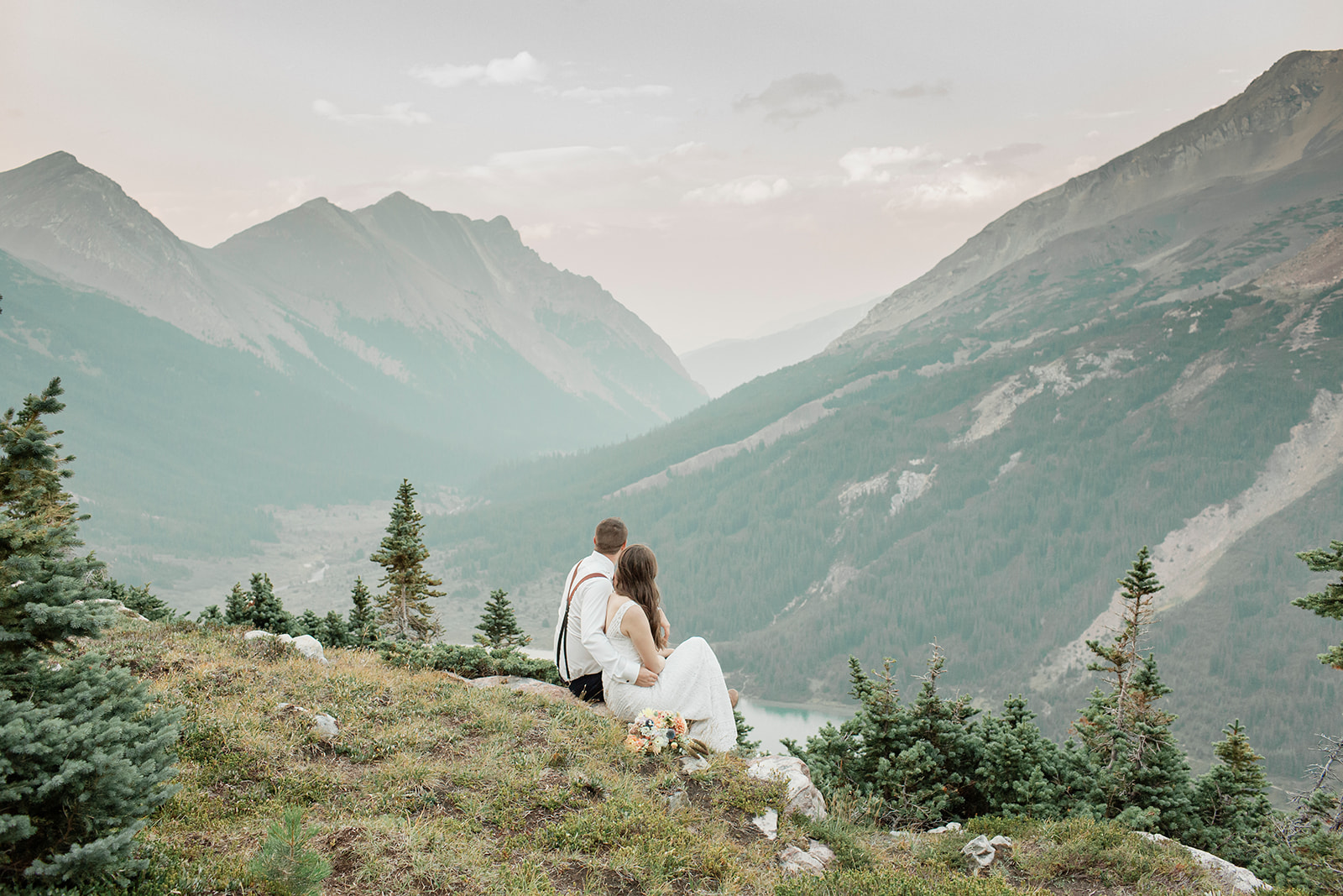 A sustainable elopement couple embraces while sitting on an overlook in Alberta. 