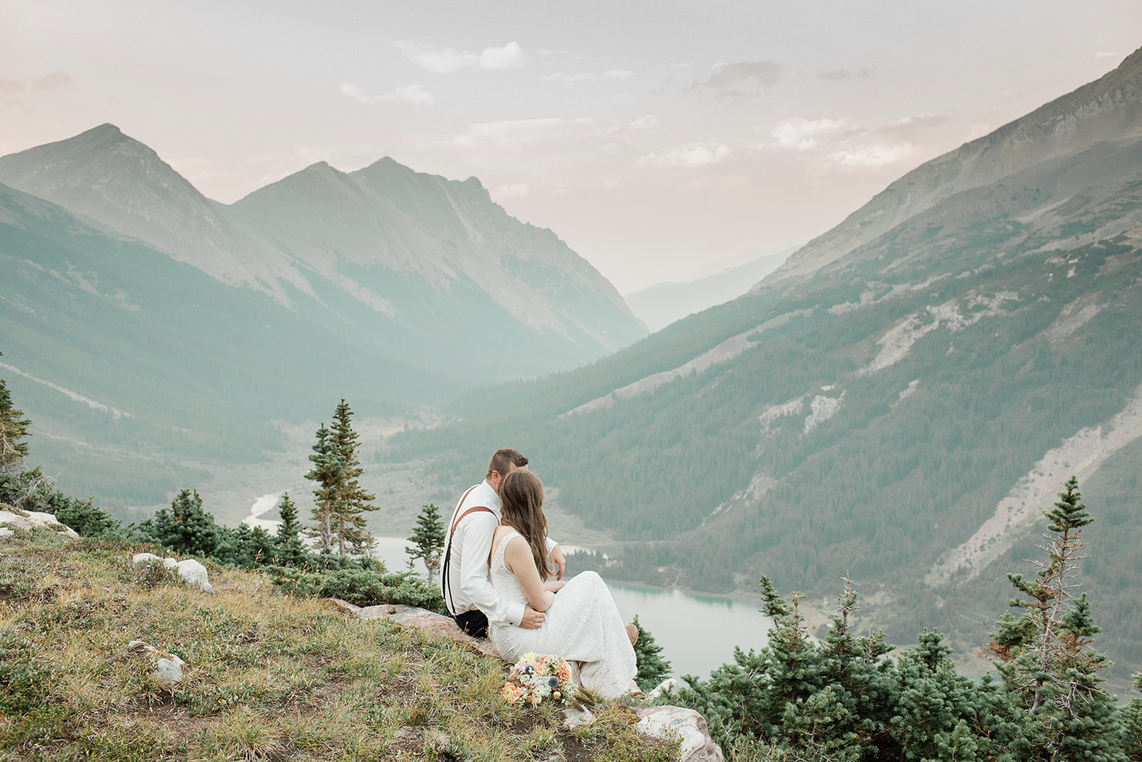 A sustainable elopement couple embraces while sitting on an overlook in Alberta. 