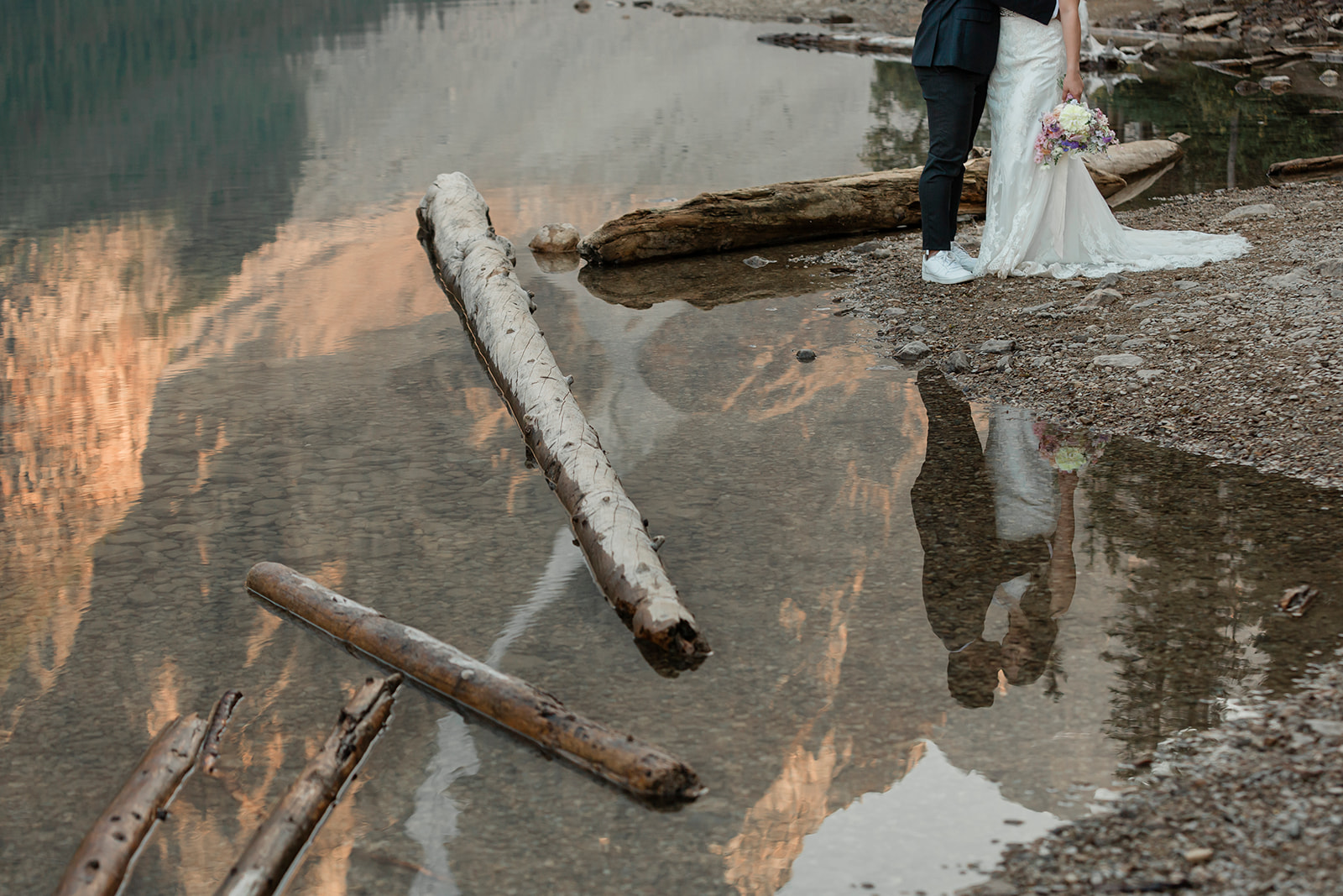 An Alberta elopement couple dressed in formal wedding stands on the shores of Moraine Lake during wedding portraits. 