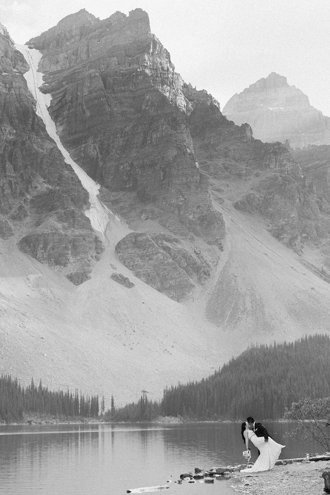 A groom dips his bride during their vow ceremony in Banff National Park near a lake.  