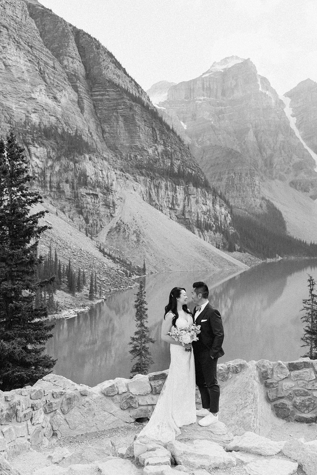 A bride and groom dressed in formal wedding attire pose for wedding portraits in front of an alpine lake in Banff. 