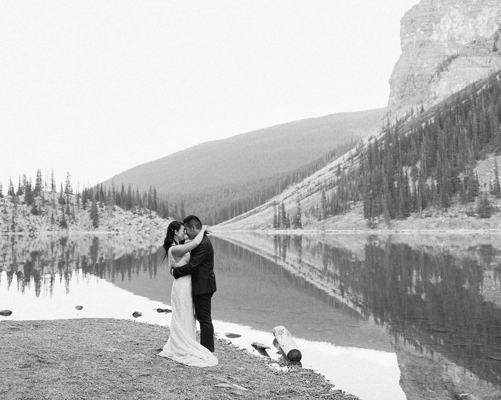 A bride and groom dressed in formal wedding attire embrace during wedding portraits in front of Moraine Lake in Banff National Park.