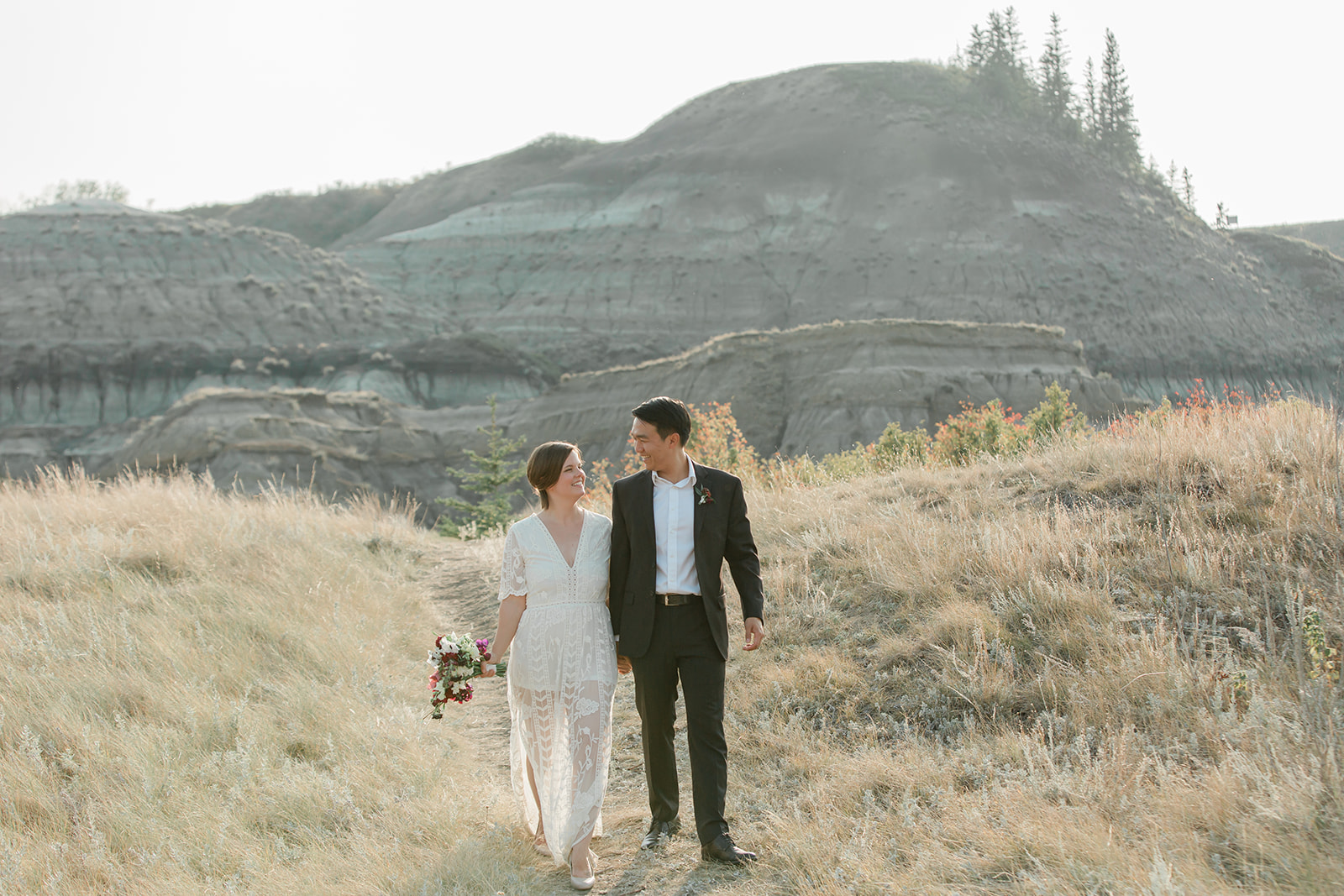 A woman dressed in a white wedding gown holds her groom's hand while walking through Horsethief Canyon in Alberta, Canada.