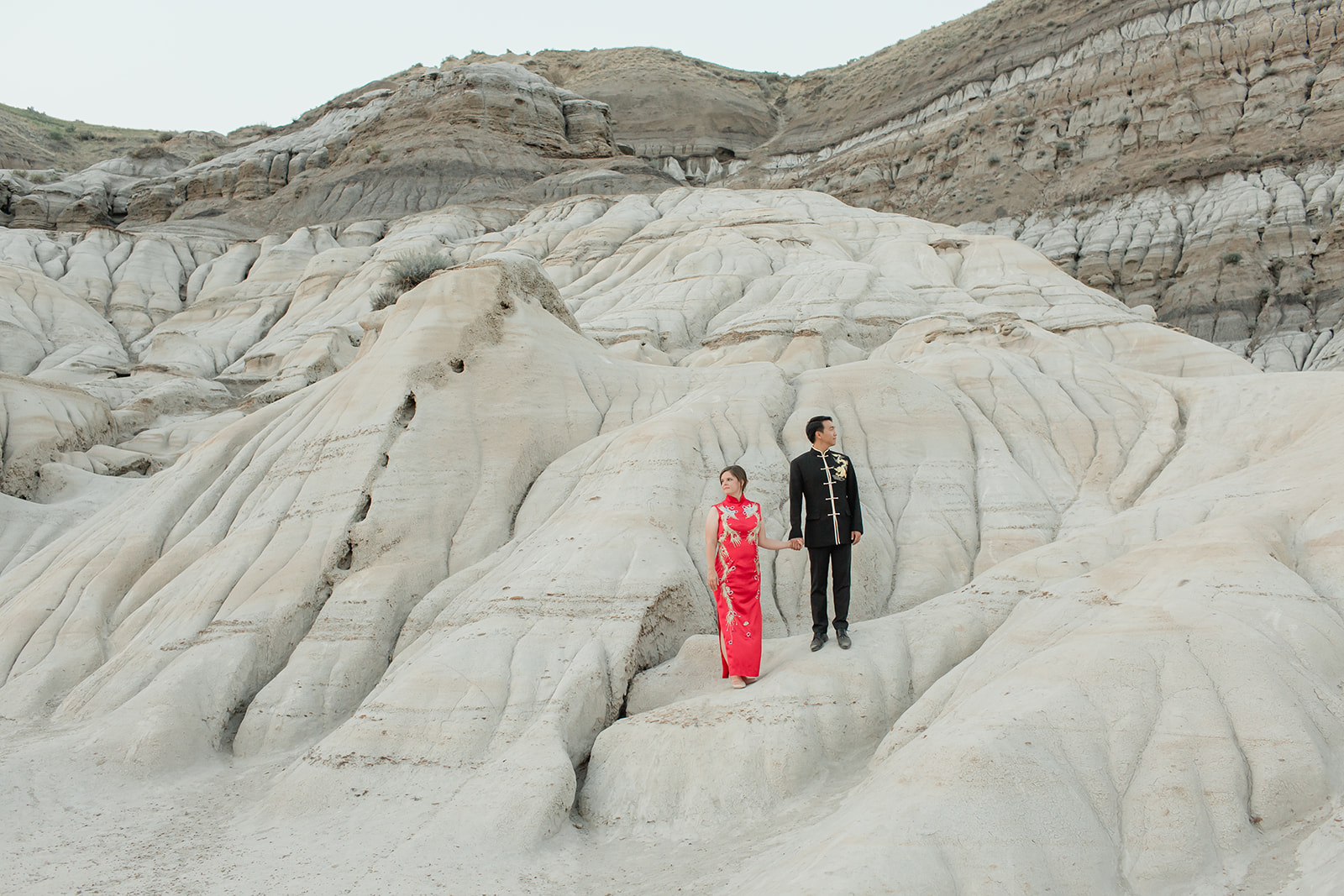 An elopement couple dressed in cultural wedding attire stares off in the distance while standing on a rock structure in Horsethief Canyon in Alberta, Canada.