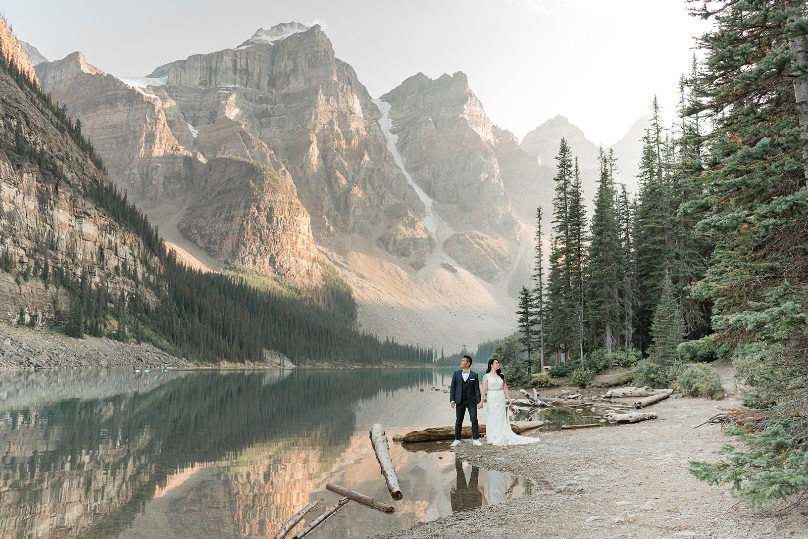 A couple holds hands during their Banff elopement near Moraine Lake and an evergreen forest.