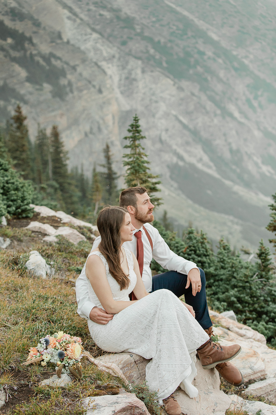 A hiking elopement couple sits on a rock that overlooks Banff National Park.