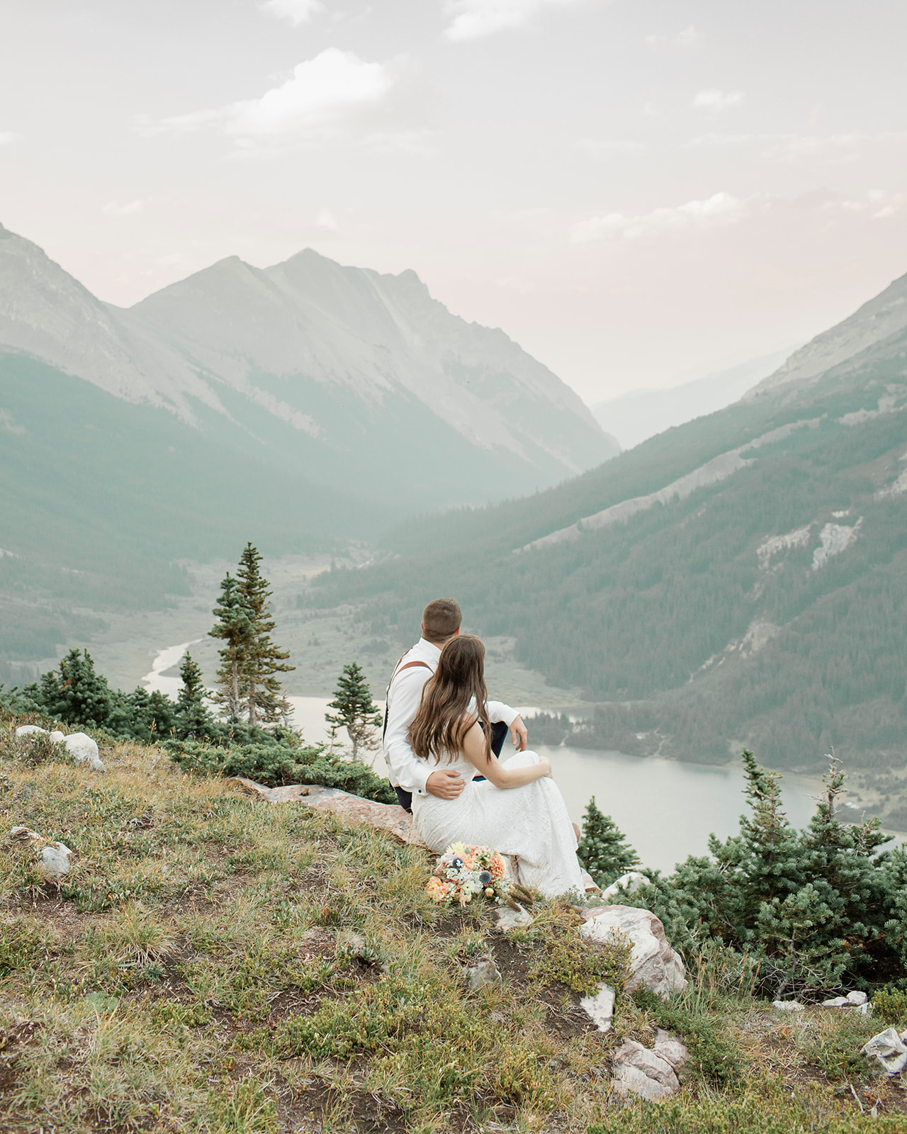 A national park elopement couple sits on a rock that overlooks Banff National Park.