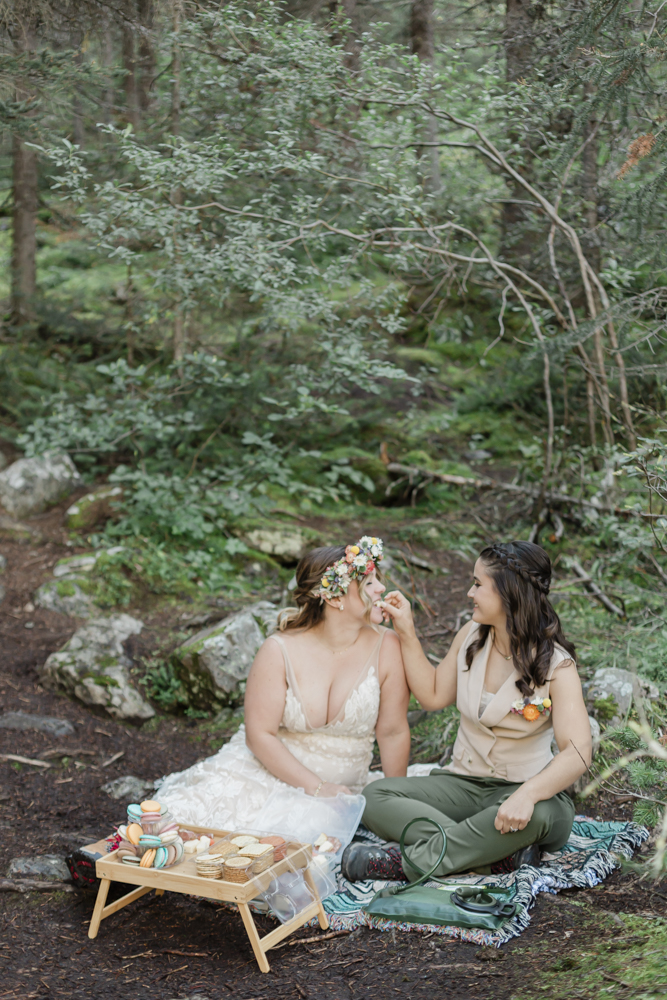 A couple enjoying a macaron and charcuterie picnic at Moraine Lake for their LGBTQ+ Banff elopement