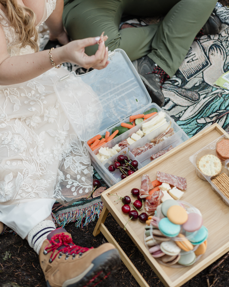 A couple enjoying a macaron and charcuterie picnic at Moraine Lake for their LGBTQ+ Banff elopement