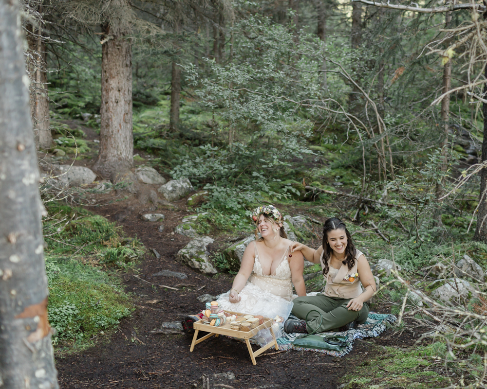 A couple enjoying a macaron and charcuterie picnic at Moraine Lake for their LGBTQ+ Banff elopement