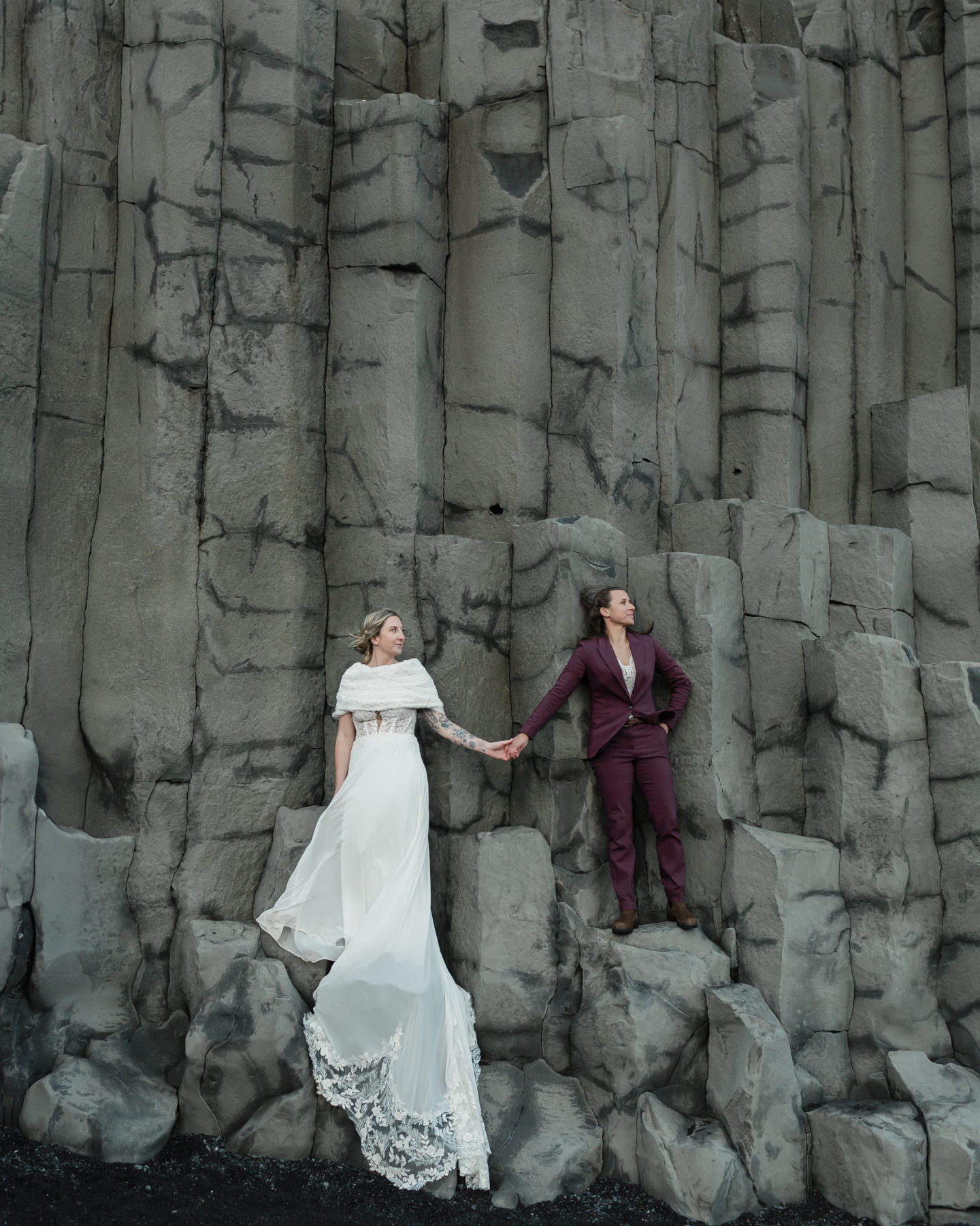 A couple holding hands and standing on the basalt columns