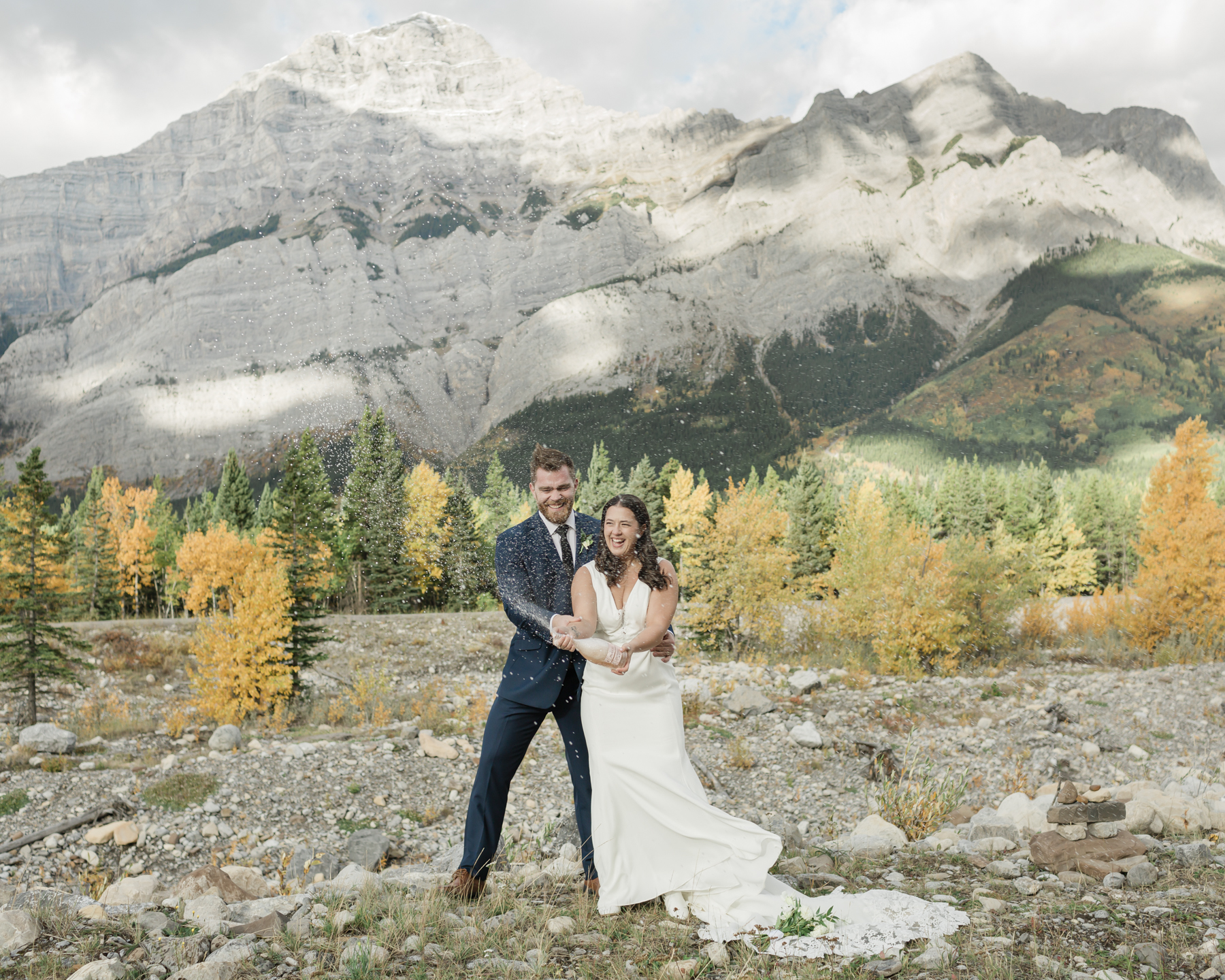 A couple celebrating with a champagne pop during their elopement near Mount Kidd