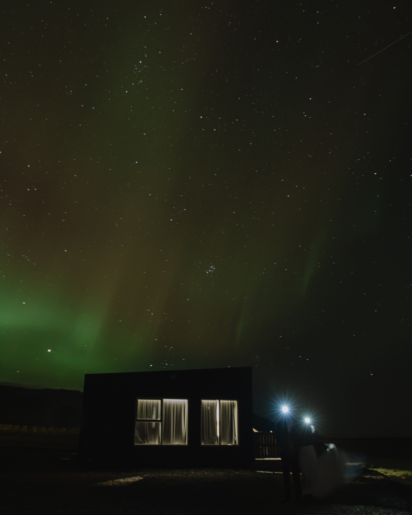 A couple posing with the Northern Lights in the background in the shoulder season in Iceland