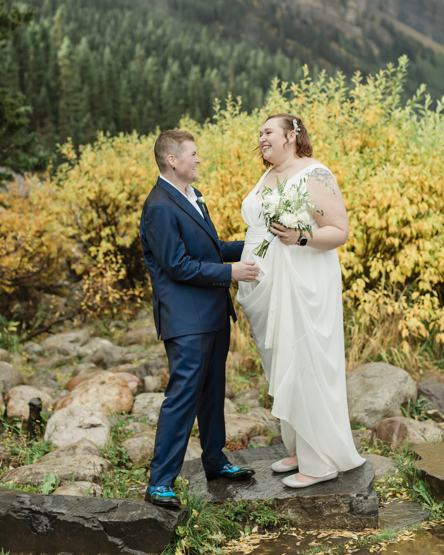 A LGBTQIA+ couple laughing together at Lake Louise in autumn