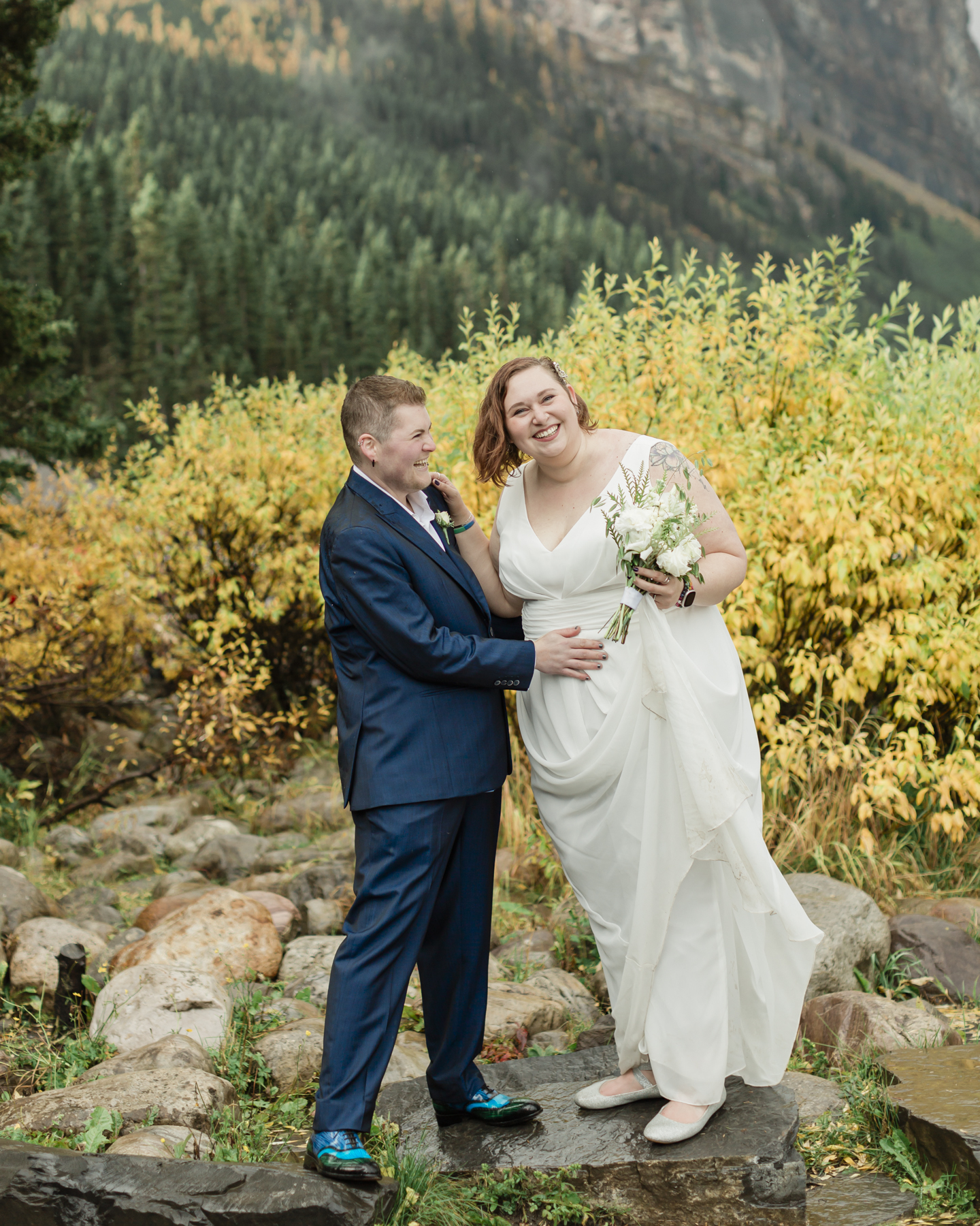 A LGBTQIA+ couple laughing together at Lake Louise in autumn