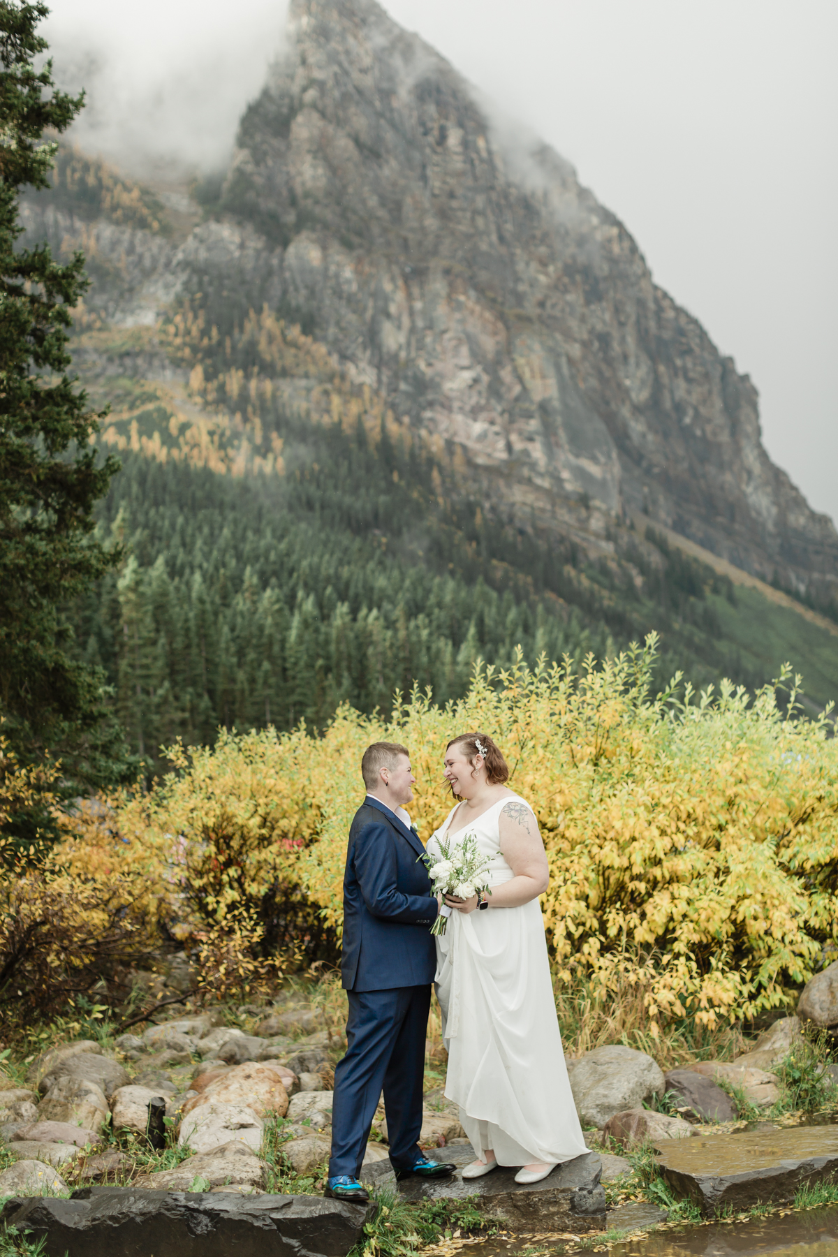 A LGBTQIA+ couple laughing together at Lake Louise in autumn